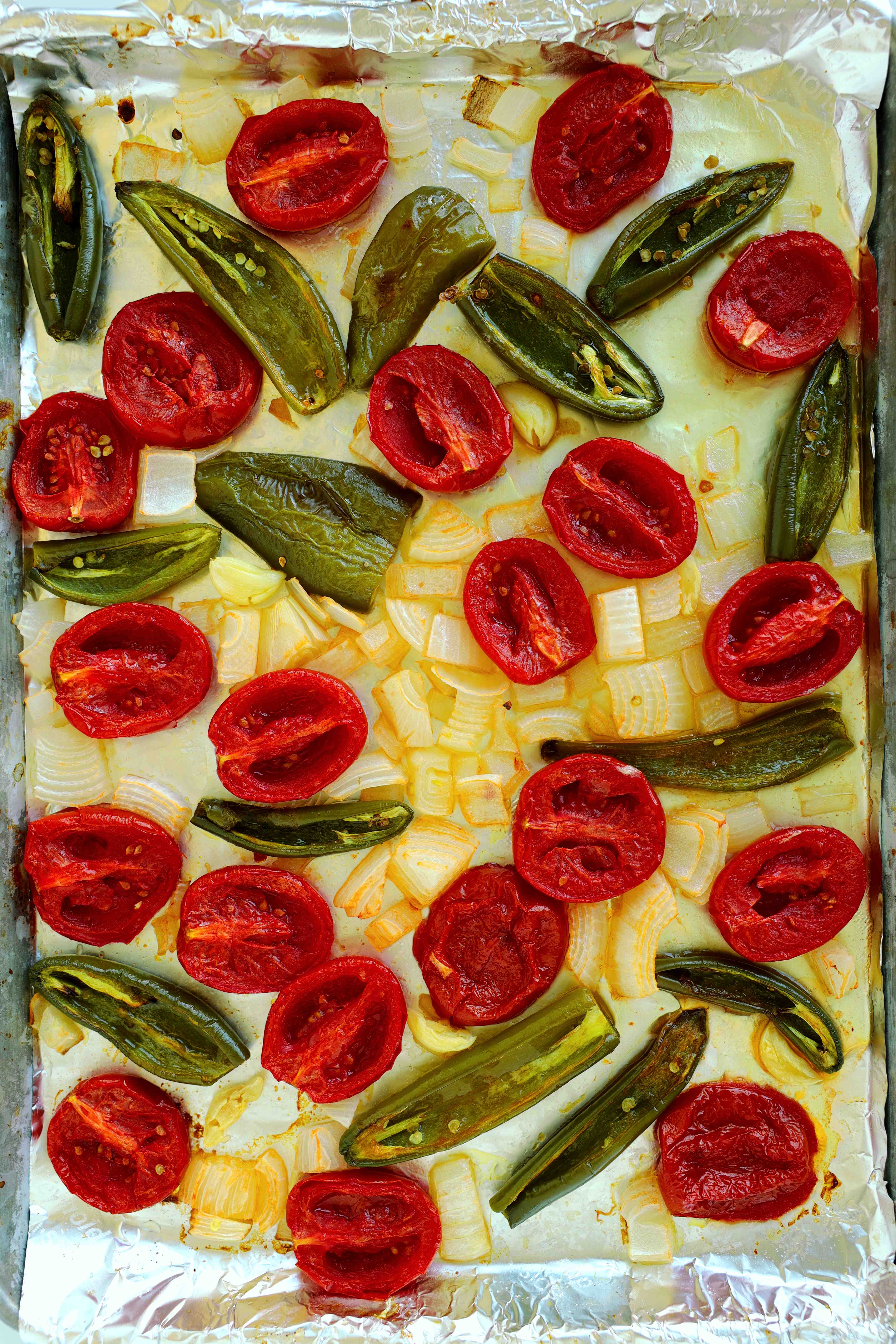 Oven-roasted tomatoes, jalapenos, and onions on a baking sheet for salsa ranchera