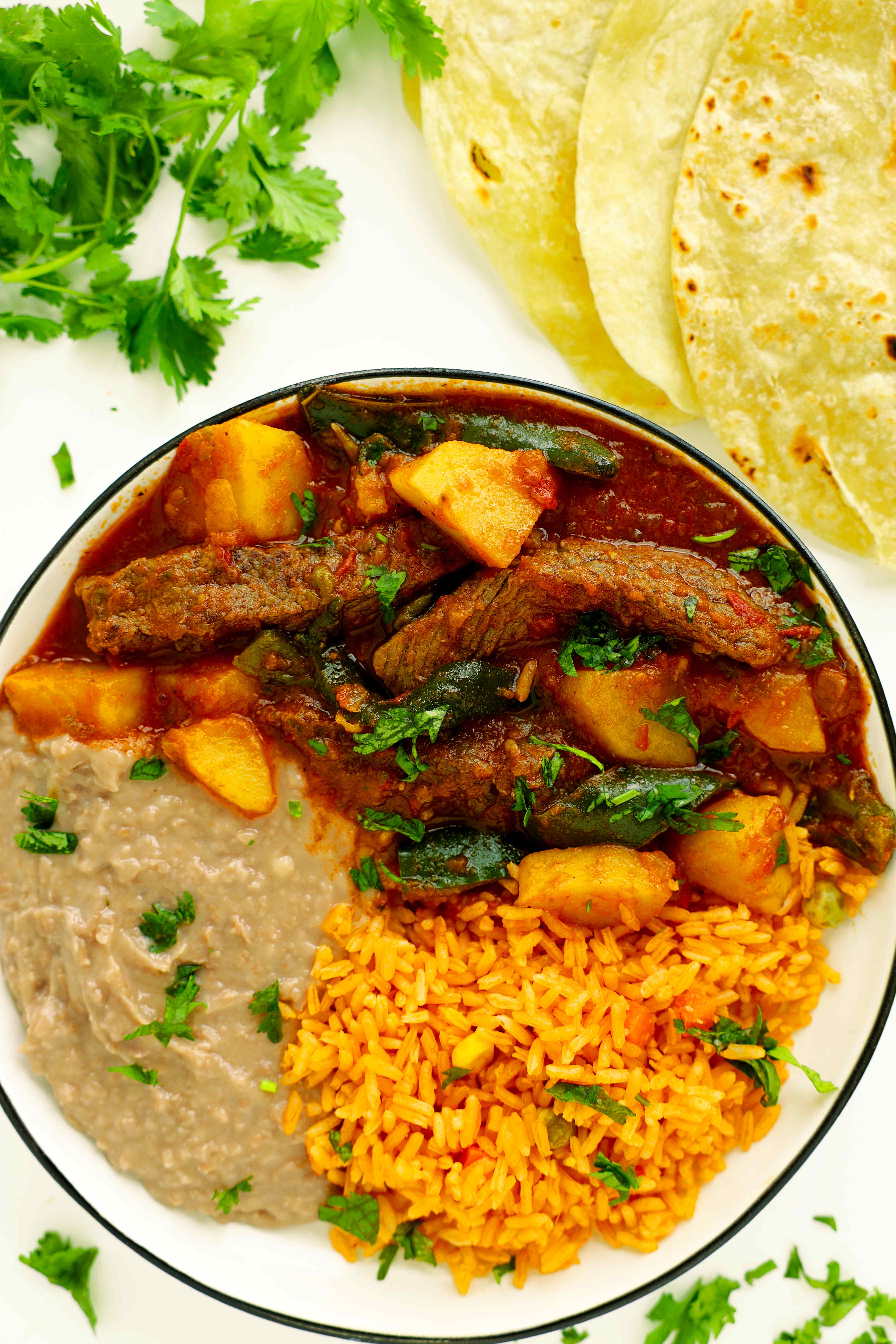 Overhead shot of Bistec Ranchero with refried beans, Mexican rice, and flour tortillas