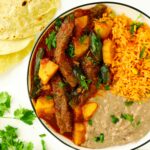 Overhead shot of Bistec Ranchero with refried beans, Mexican rice, and flour tortillas