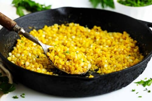 Fried corn in a cast-iron skillet with a serving spoon