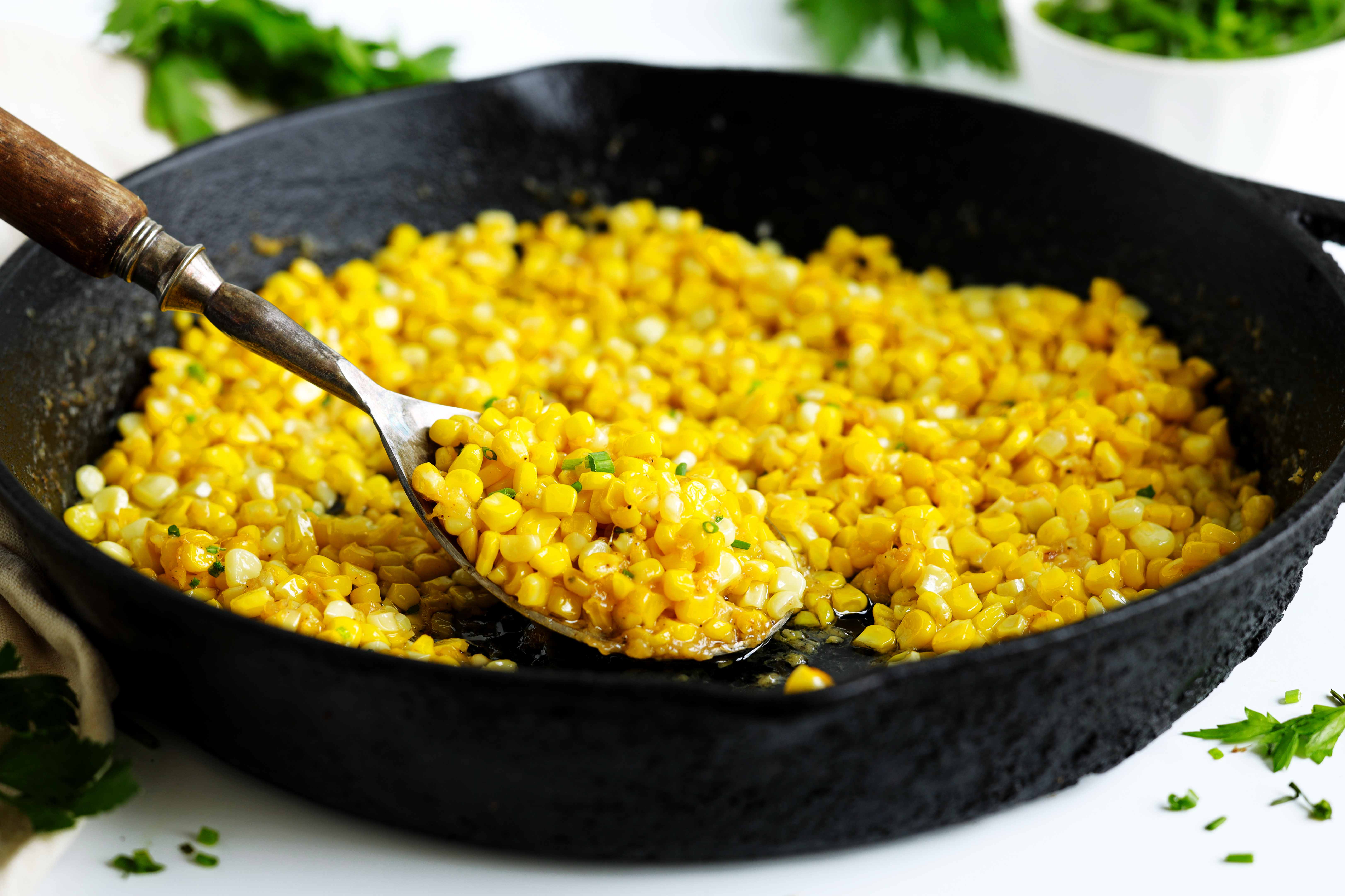 Fried corn in a cast-iron skillet with a serving spoon