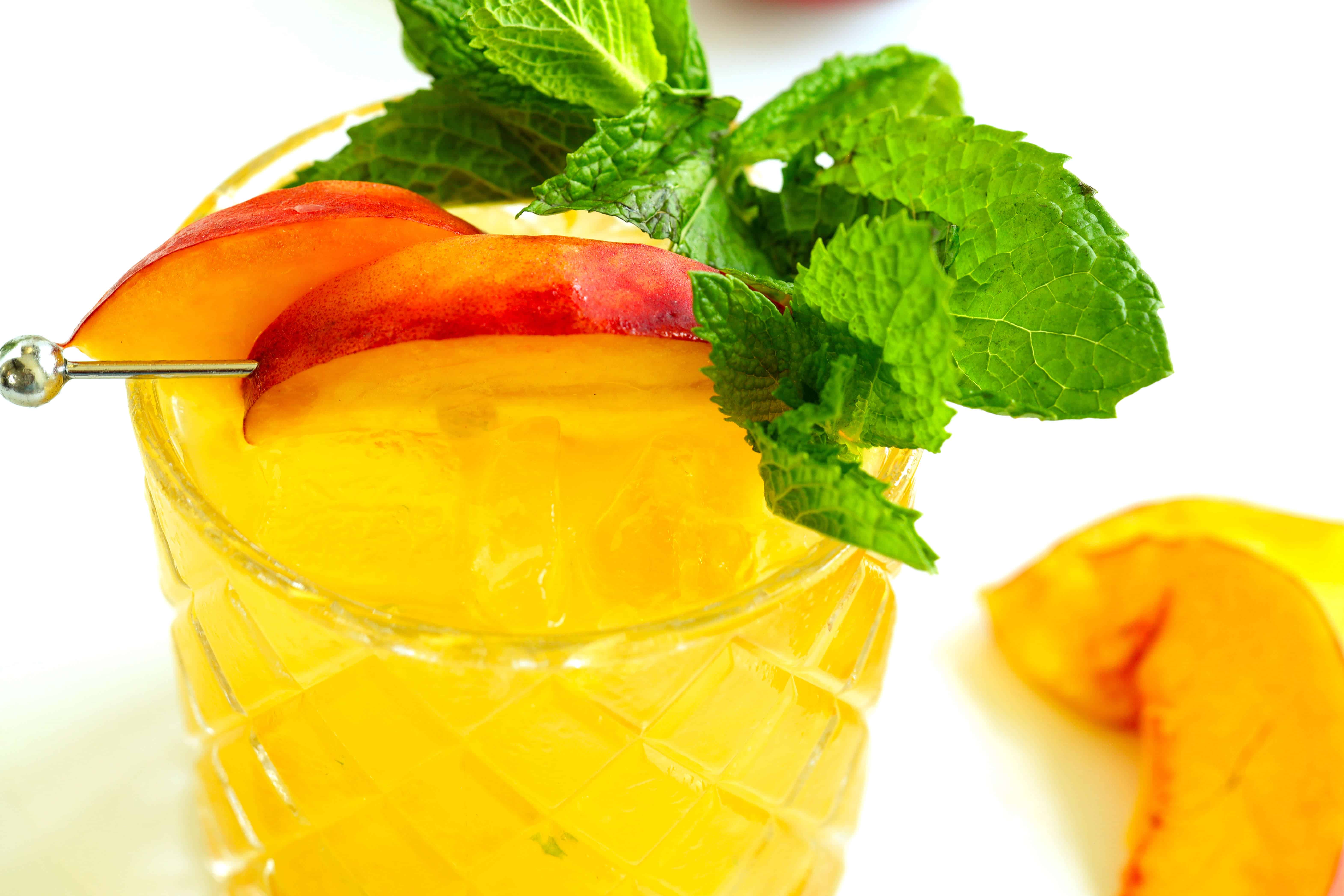 Closeup of Peach Bourbon Smash cocktail garnished with peach slices and fresh mint