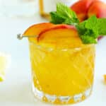 Peach Bourbon Smash cocktail garnished with peach slices and fresh mint