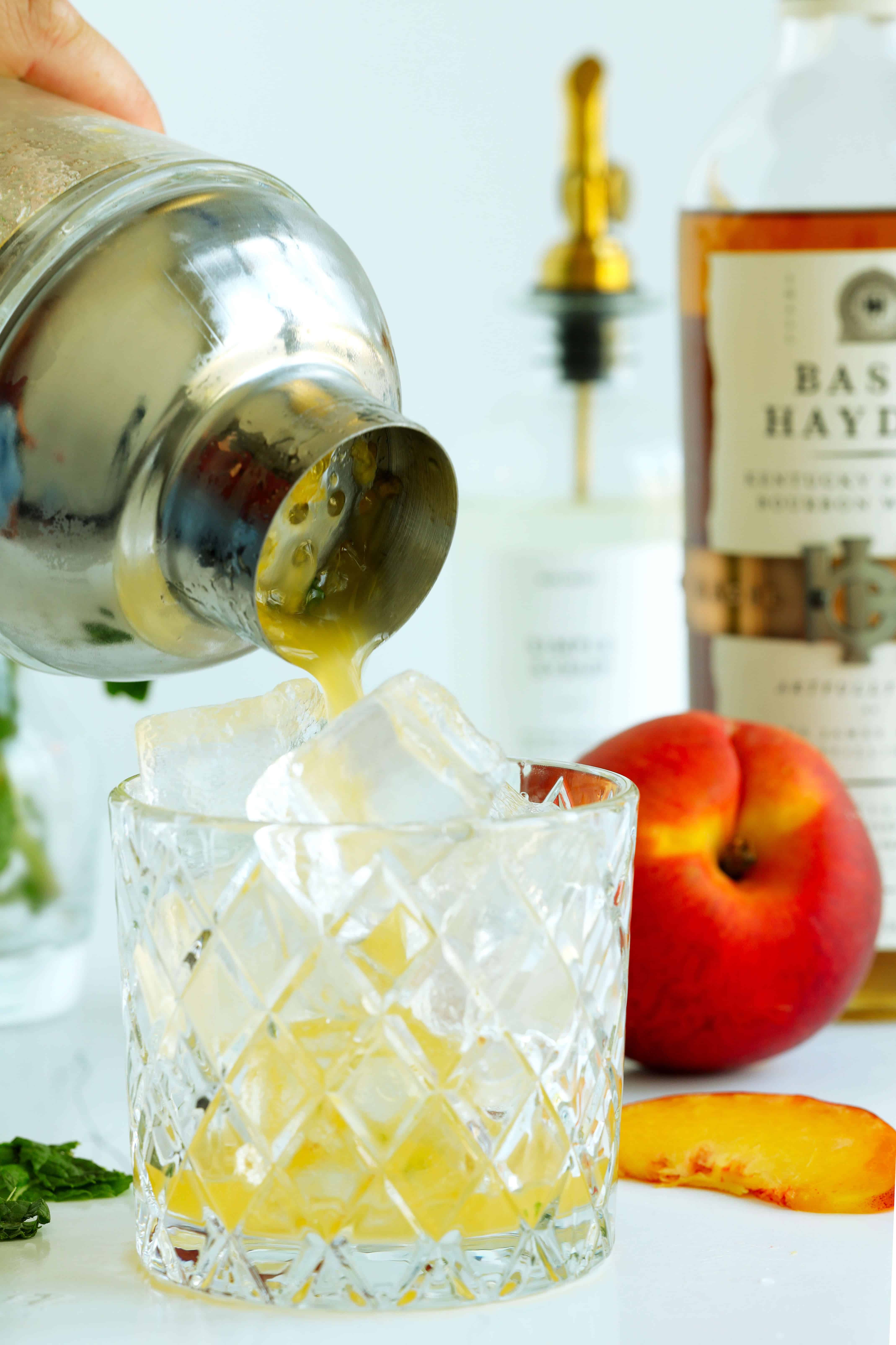 Pouring Peach Bourbon Smash ingredients out of a shaker into rock glass with ice