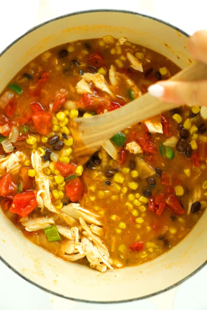 Stirring Chicken Enchilada Soup ingredients in a Dutch oven