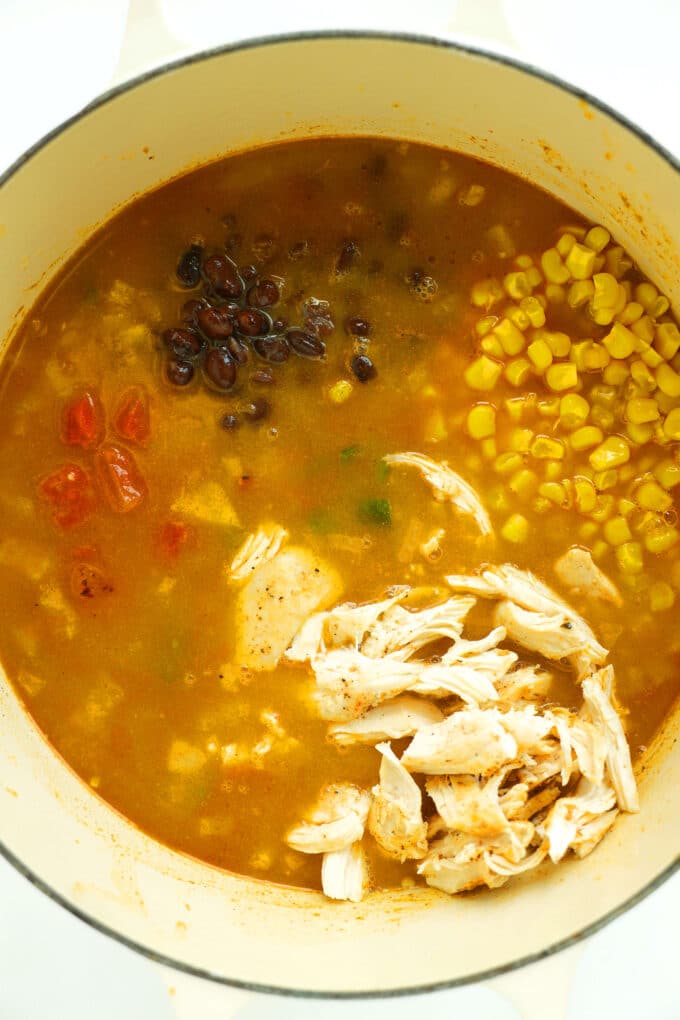 Shredded chicken, corn, black beans, fire-roasted tomatoes added to Dutch oven for Chicken Enchilada Soup