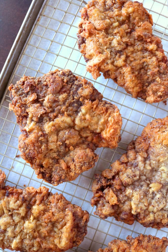 Crispy golden-brown chicken fried steaks cooling on a wire rack over a baking sheet, showing a crunchy, textured breading.