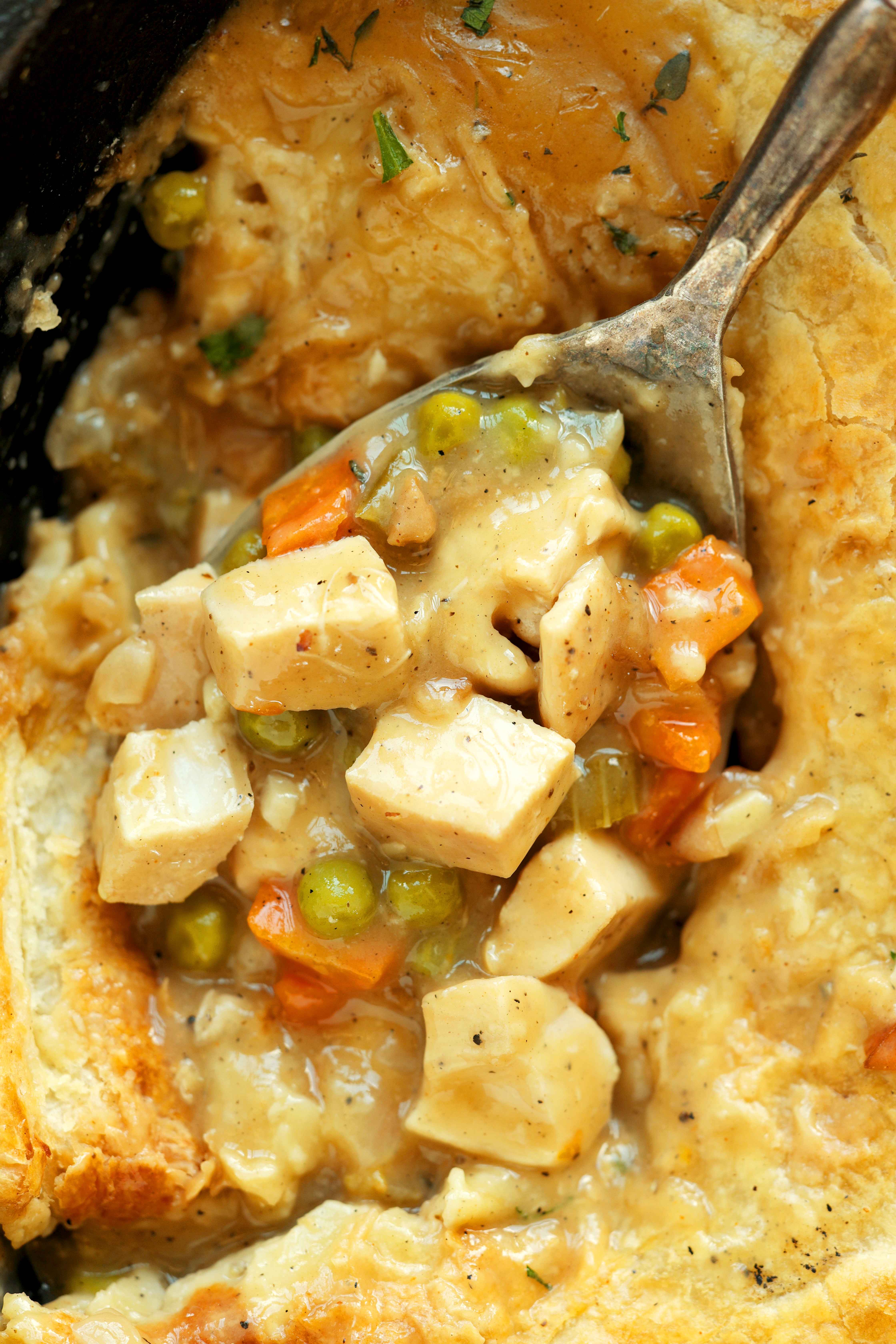 Overhead, close-up shot of Chicken Pot Pie with Puff Pastry with a spoon in a cast iron skillet