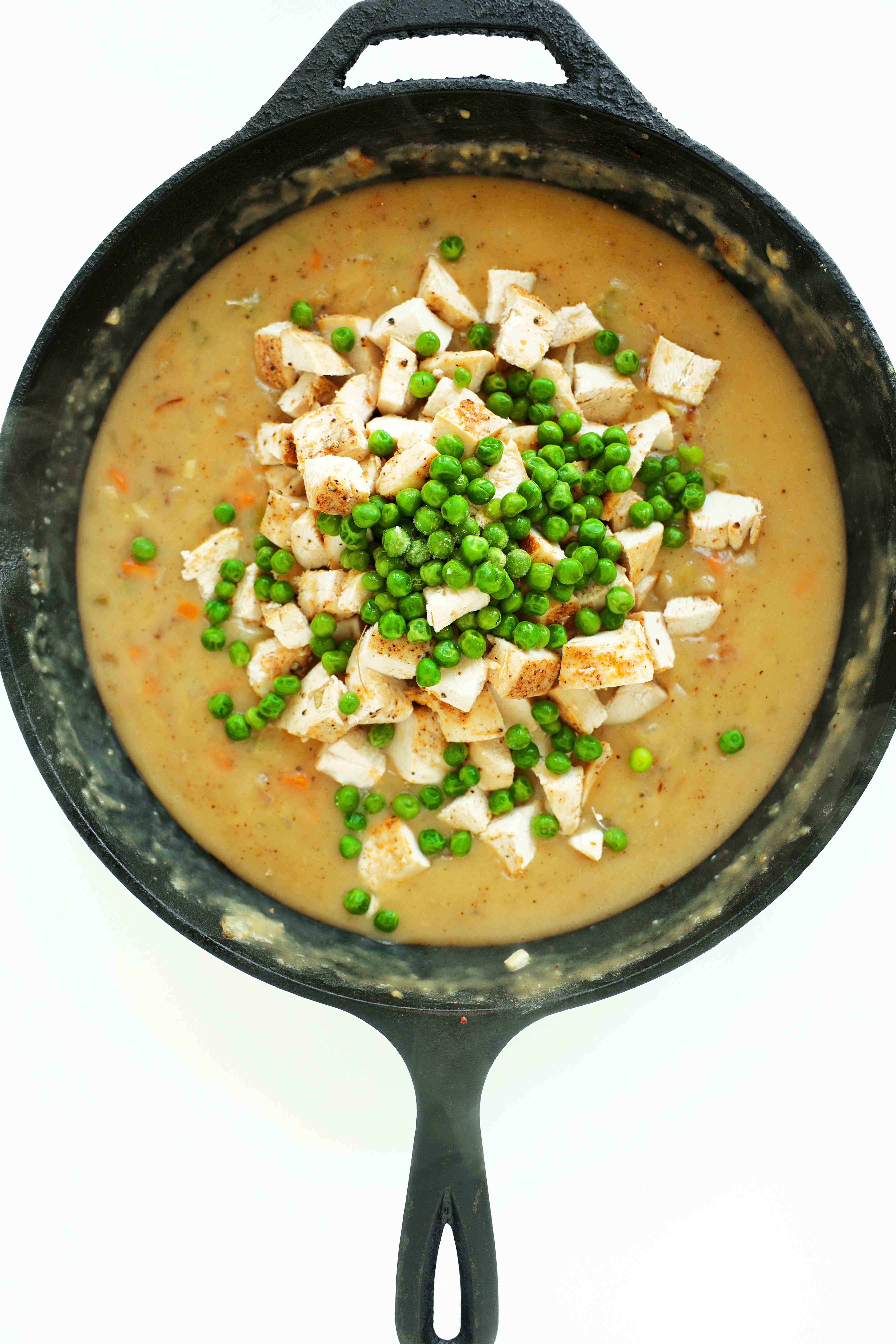 Adding peas and diced chicken to the filling components of the Chicken Pot Pie with Puff Pastry in a cast iron skillet