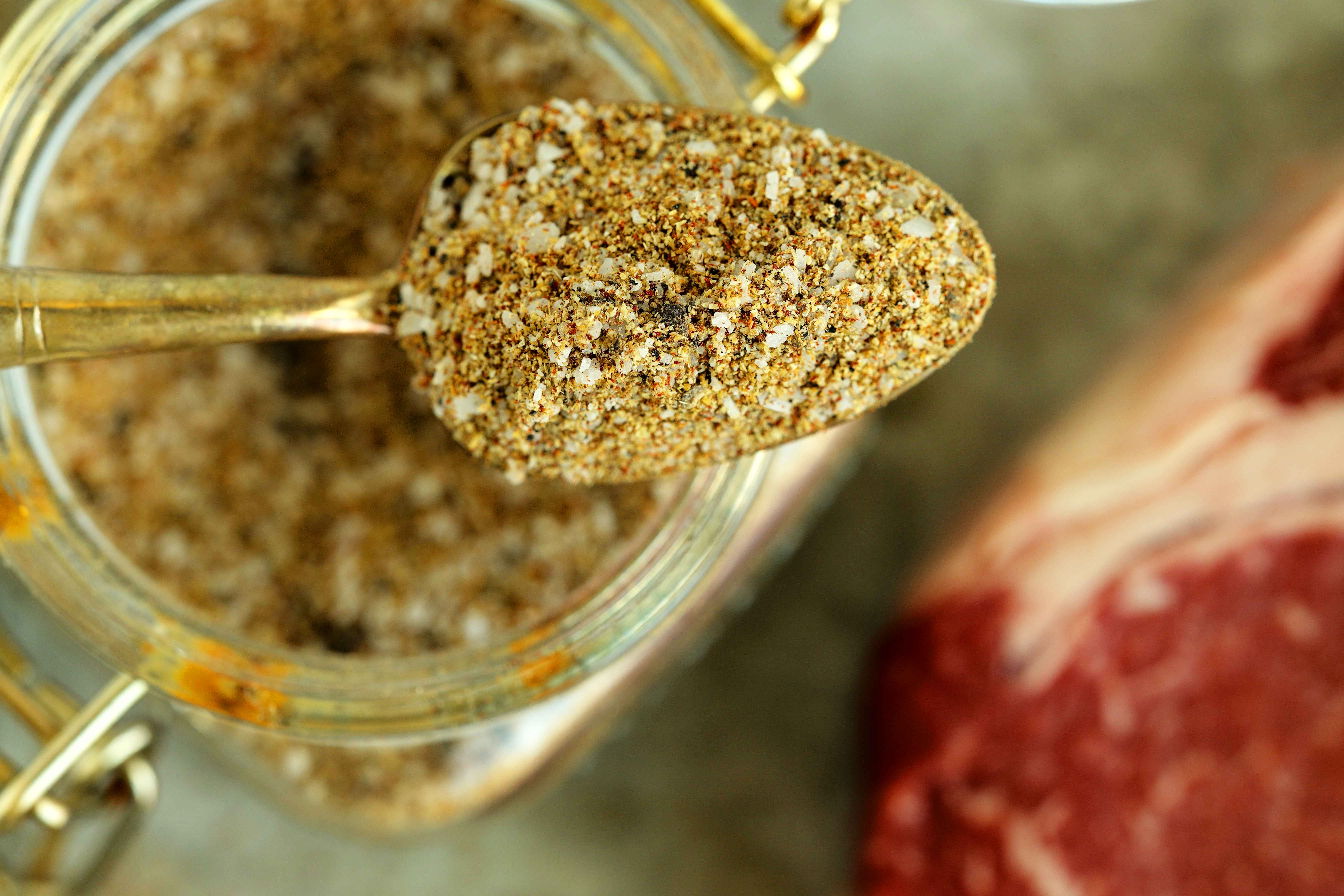 Overhead shot of steak seasoning in a glass storage container and a spoon