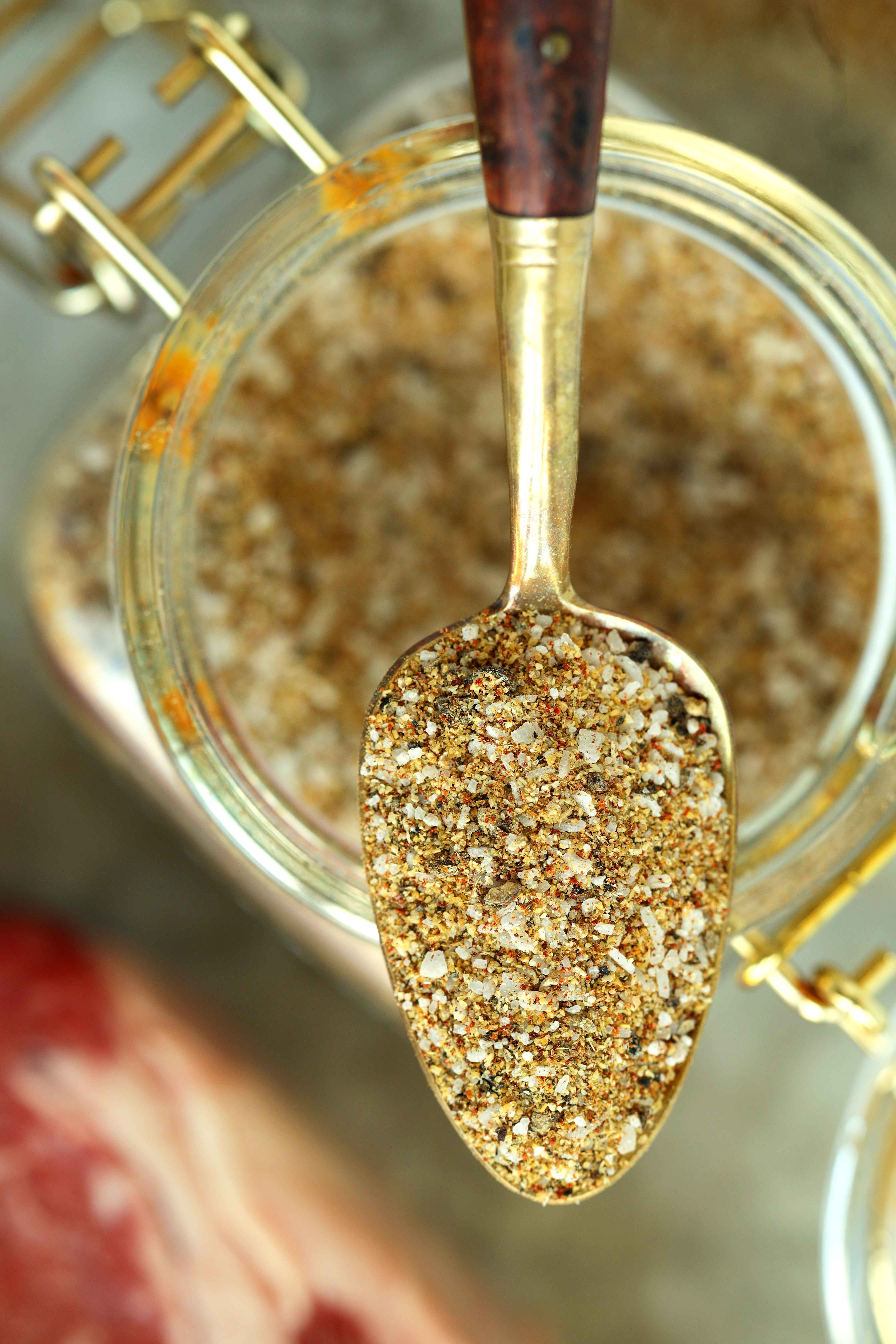 Overhead shot of steak seasoning in a glass storage container and a spoon