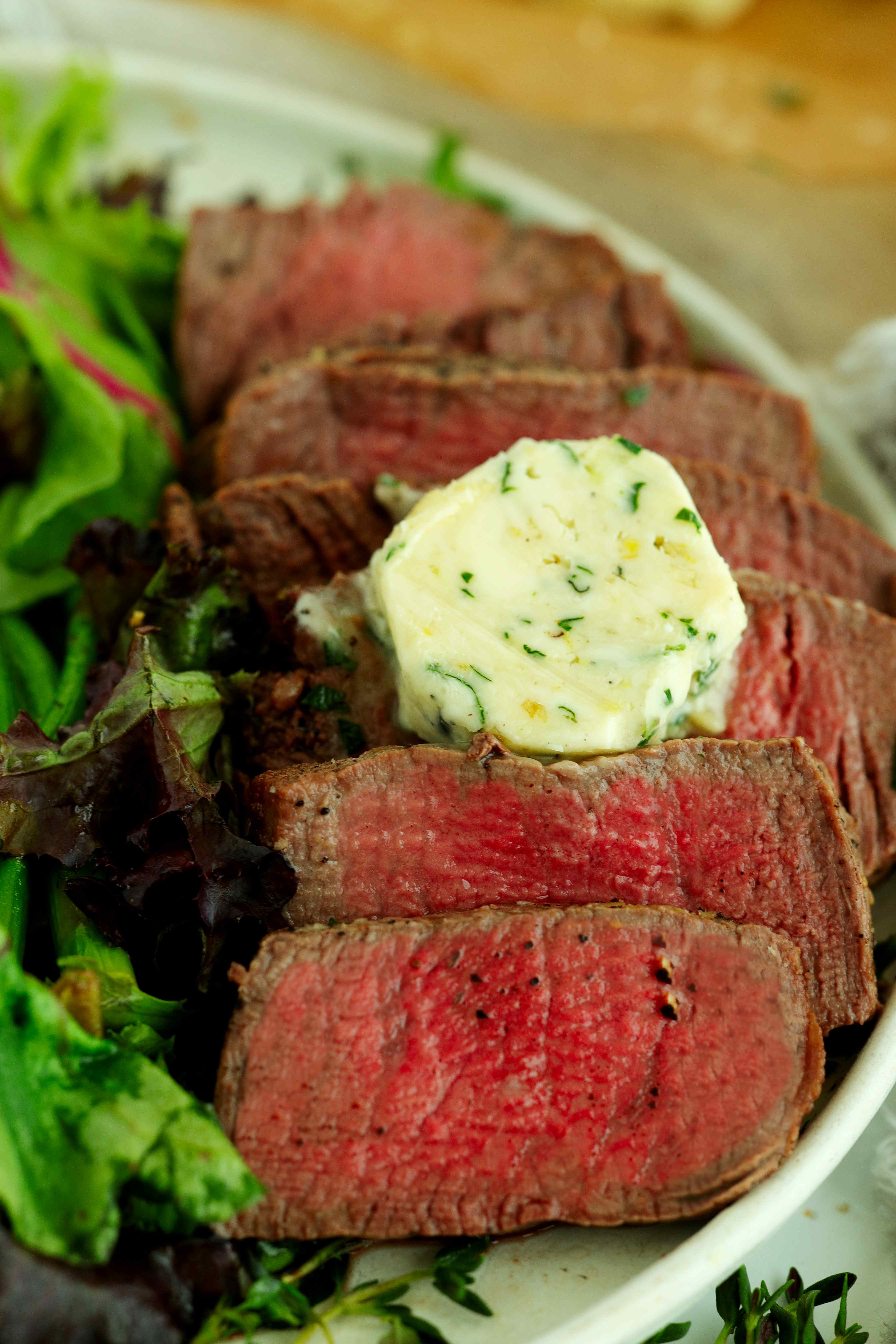 Sliced medium-rare filet mignon topped with a round of garlic herb butter and served with fresh greens.