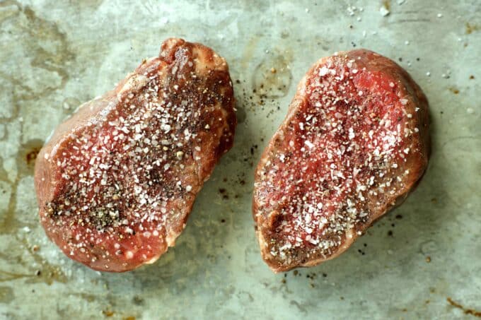 Uncooked filet mignon steaks sprinkled with coarse salt and pepper on a baking sheet