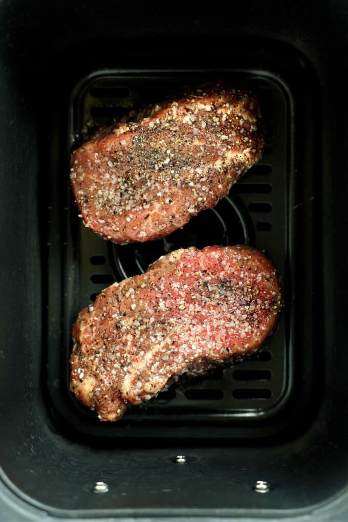 Raw filet mignon steaks seasoned with coarse salt and pepper inside an air fryer basket.