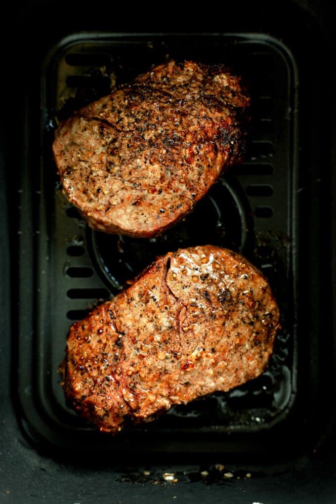 Two seared filet mignon steaks cooking in an air fryer basket.