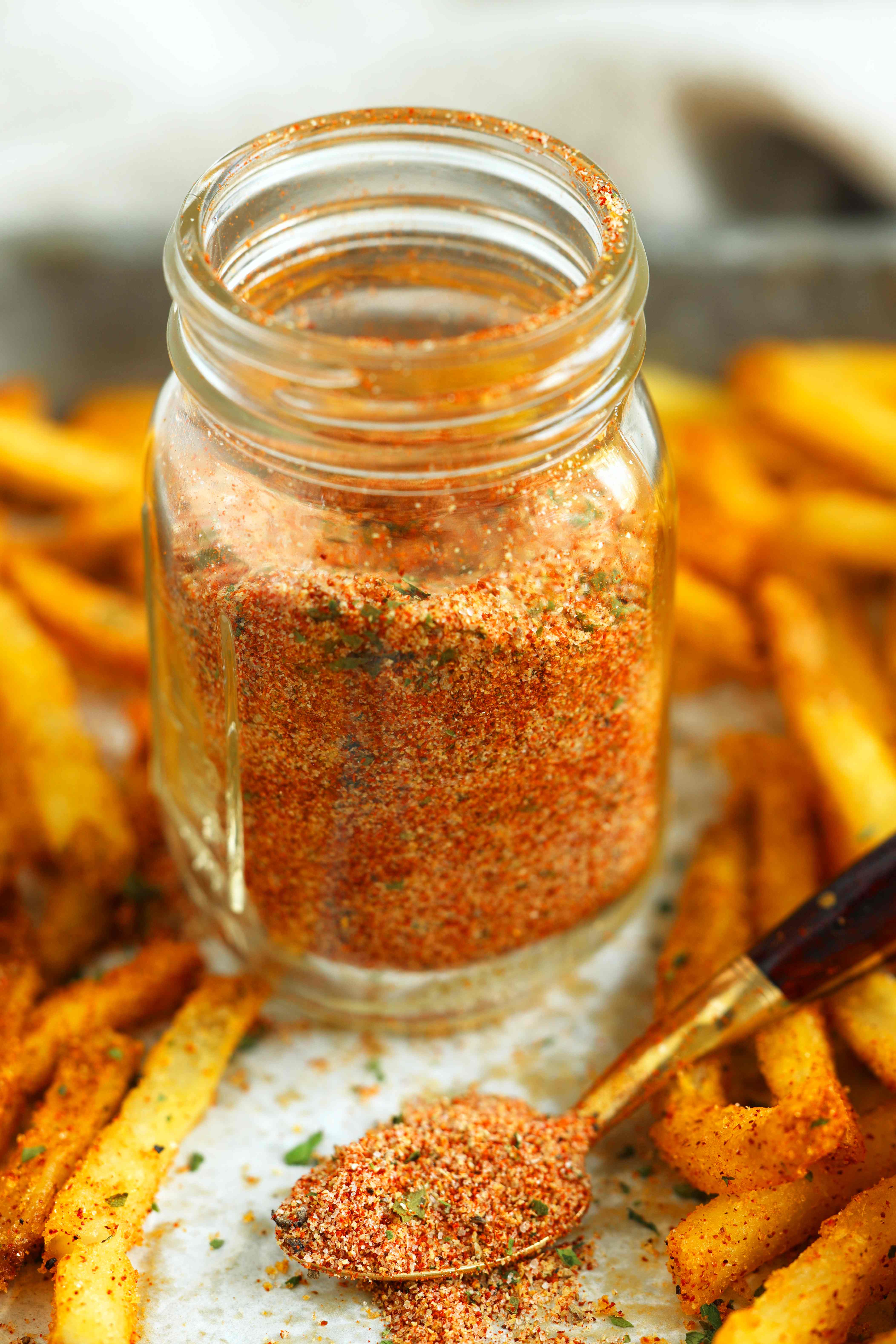 Jar of homemade fry seasoning surrounded by golden French fries, with a spoonful of the colorful spice blend in front, ready for sprinkling.