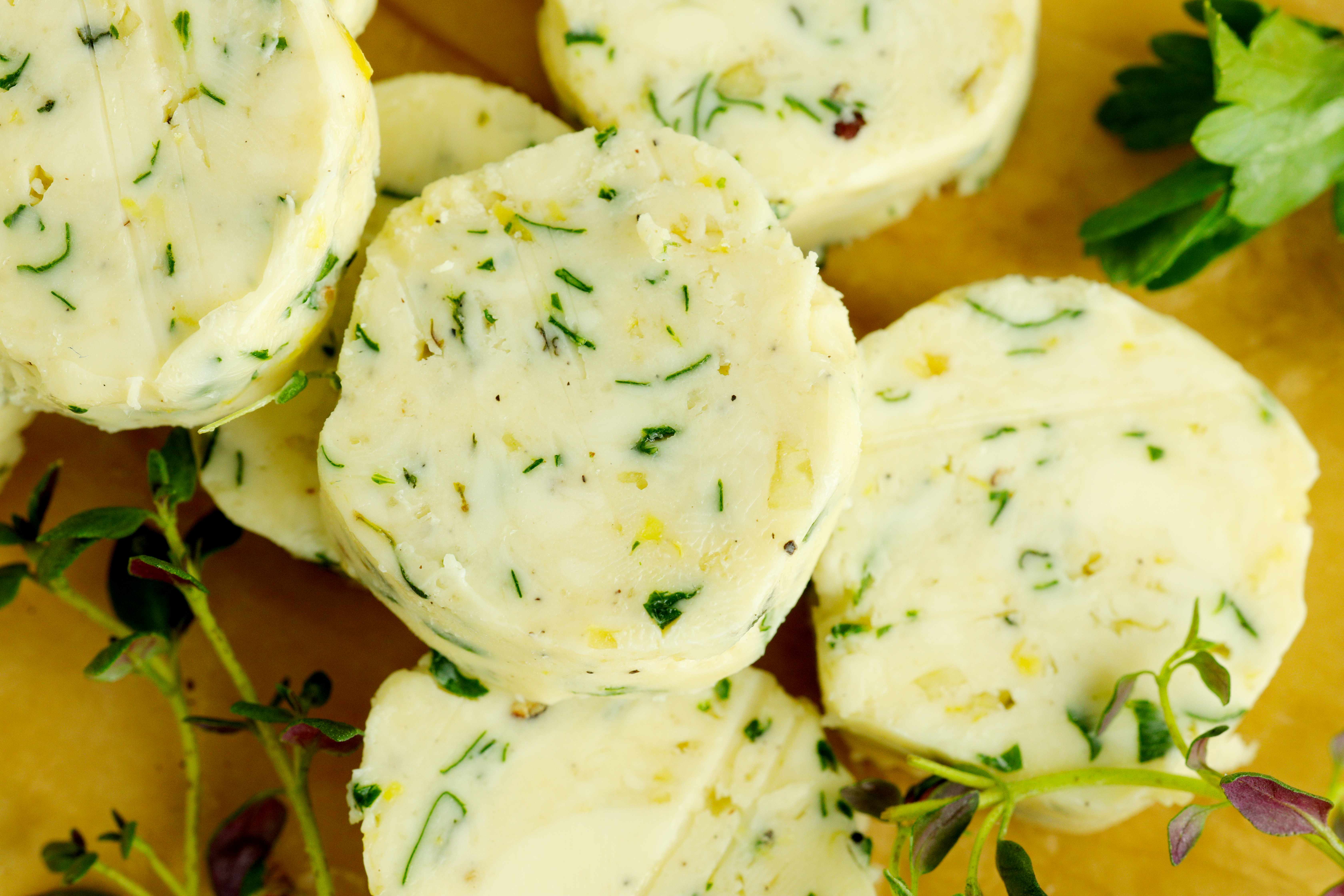 Sliced rounds of homemade herb butter with fresh parsley and thyme on parchment paper.