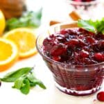 Cranberry sauce with orange juice surrounded by fresh oranges, cranberries, and mint leaves for garnish.