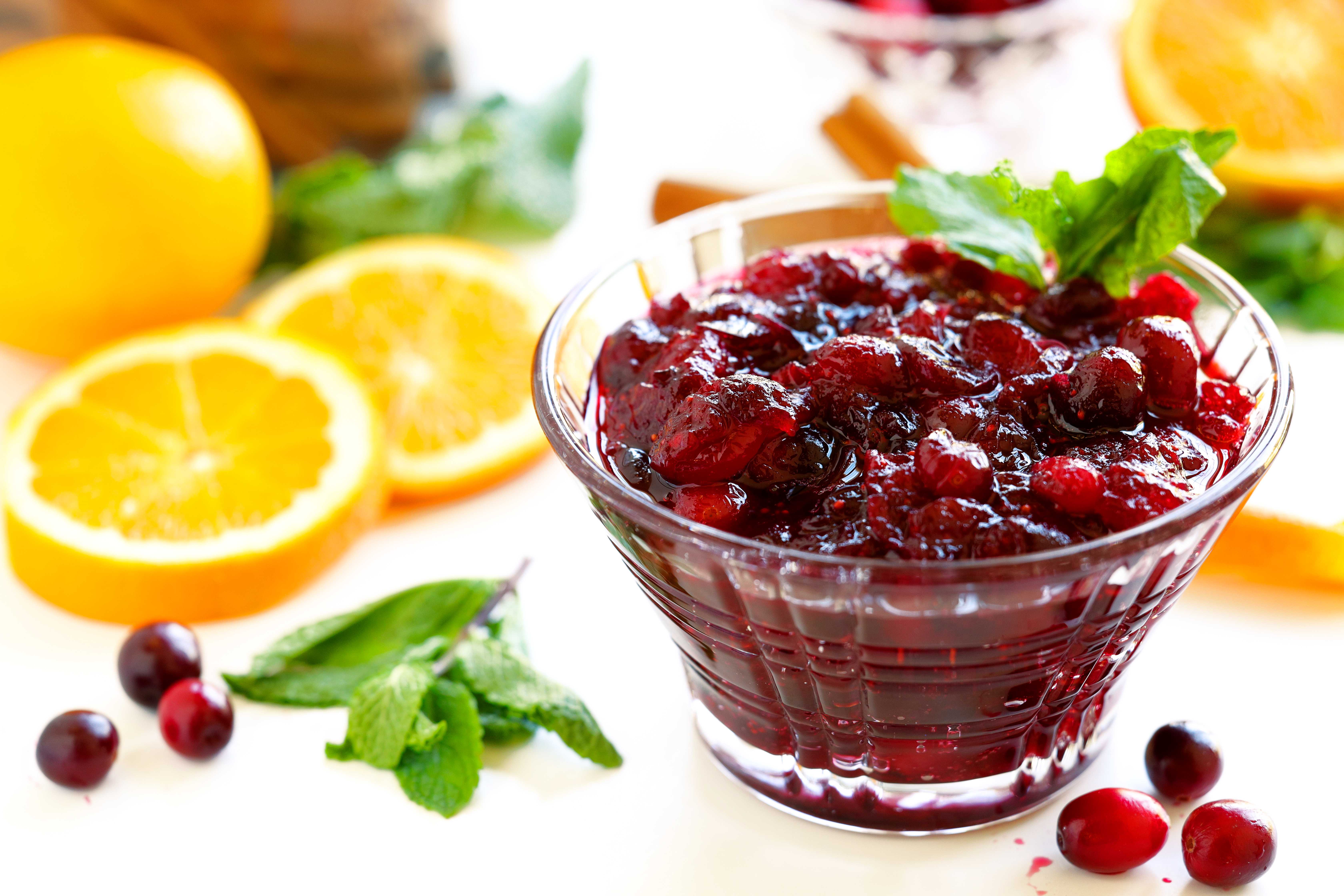 Cranberry sauce with orange juice surrounded by fresh oranges, cranberries, and mint leaves for garnish.