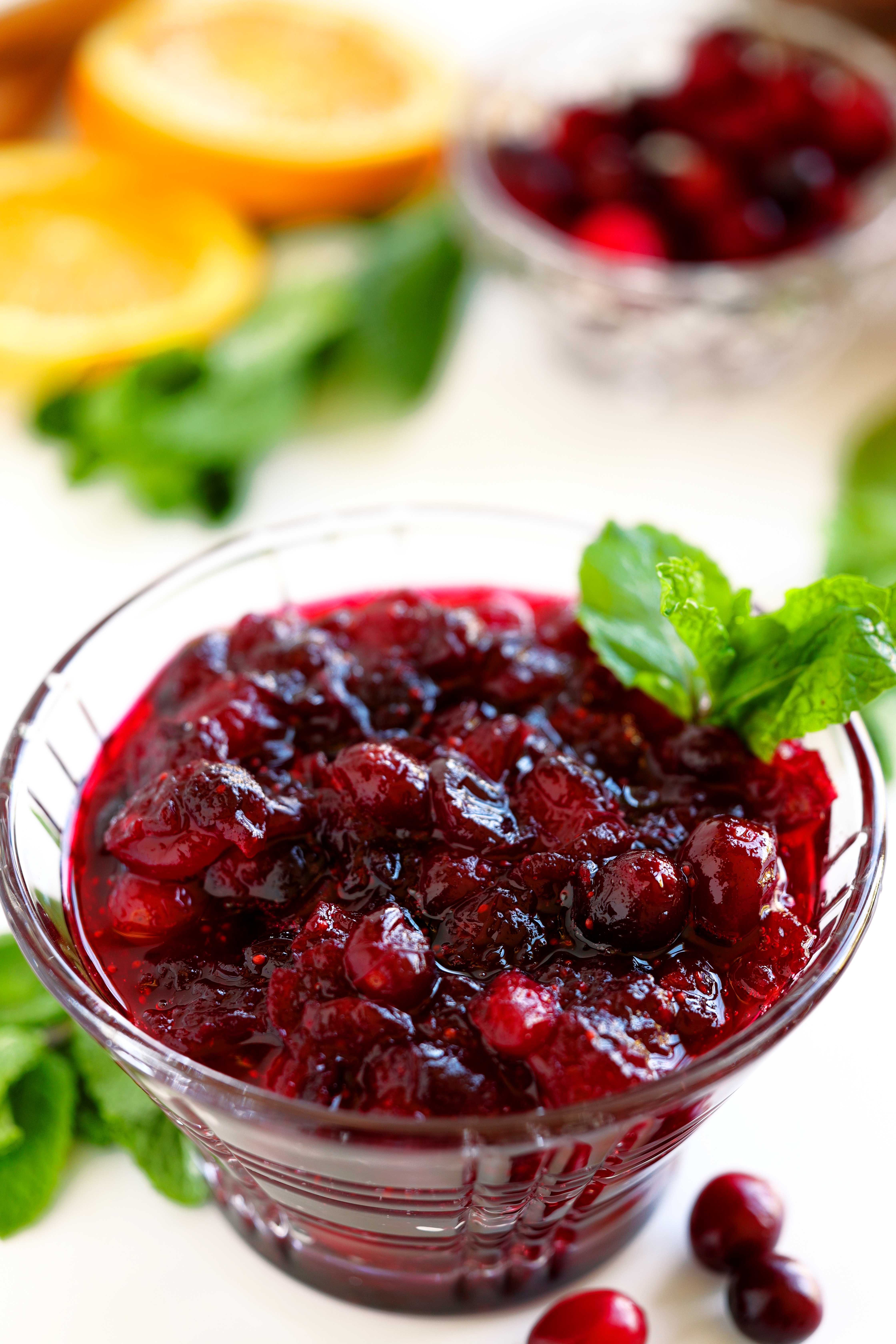 Close-up of cranberry sauce in a glass dish showing its glossy, jammy texture with a mint garnish.