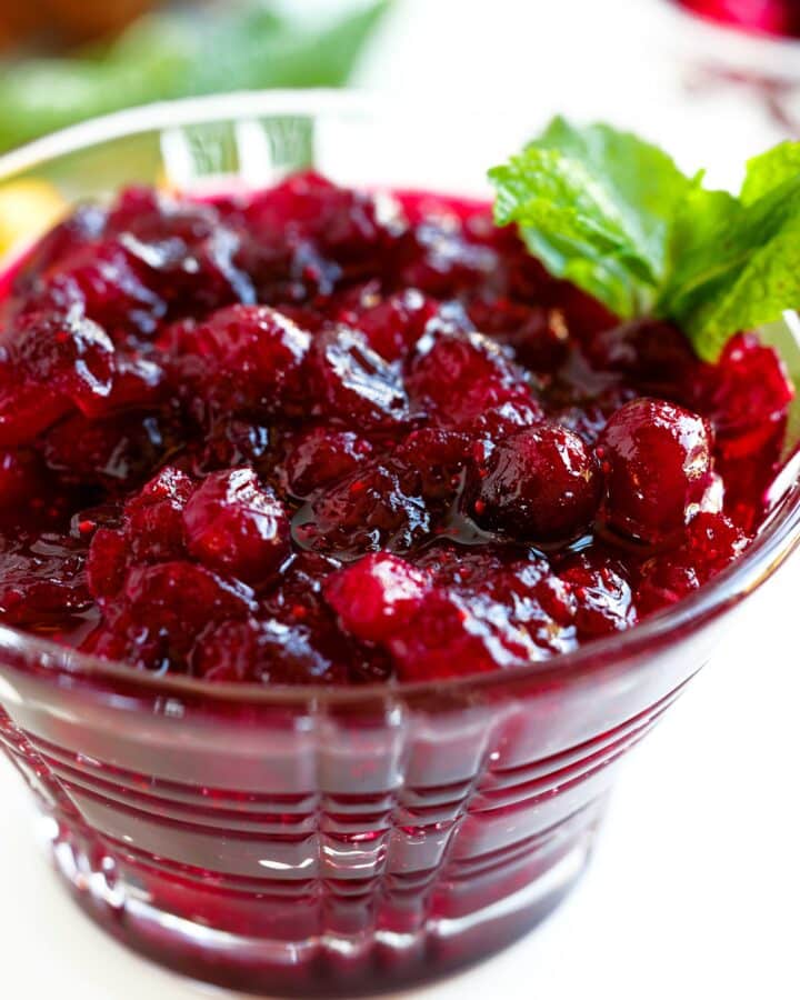 Homemade cranberry sauce with orange juice served in a glass bowl, garnished with fresh mint.