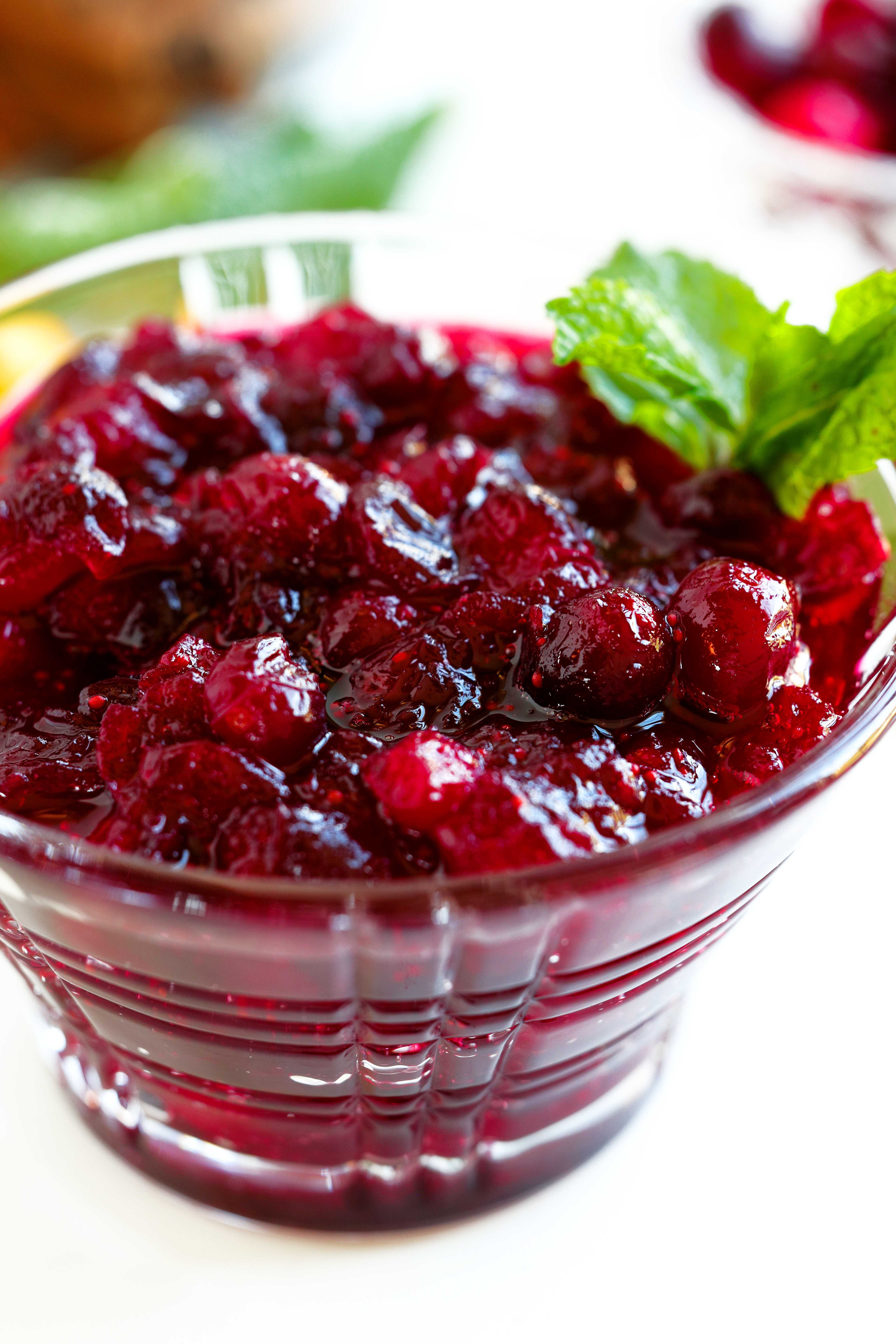 Homemade cranberry sauce with orange juice served in a glass bowl, garnished with fresh mint.
