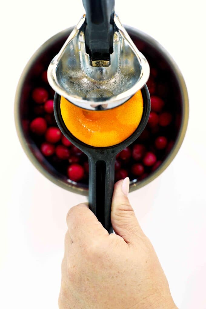 Orange halves being juiced over cranberries for homemade cranberry sauce with fresh orange juice.