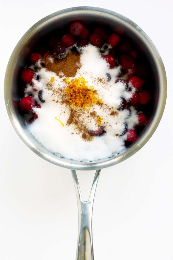 Fresh cranberries coated in sugar inside a saucepan for homemade cranberry sauce with orange juice.
