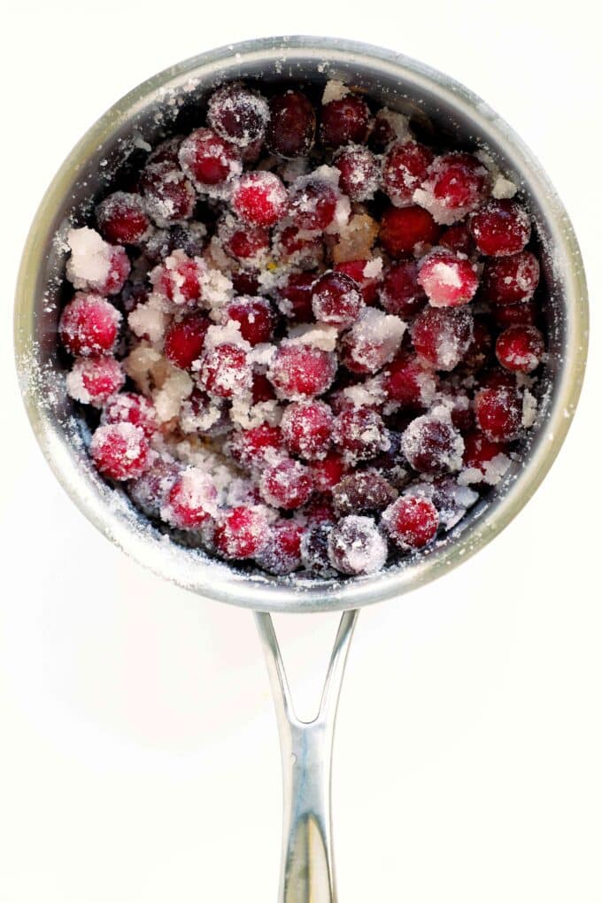 Fresh cranberries coated in sugar inside a saucepan for homemade cranberry sauce with orange juice.
