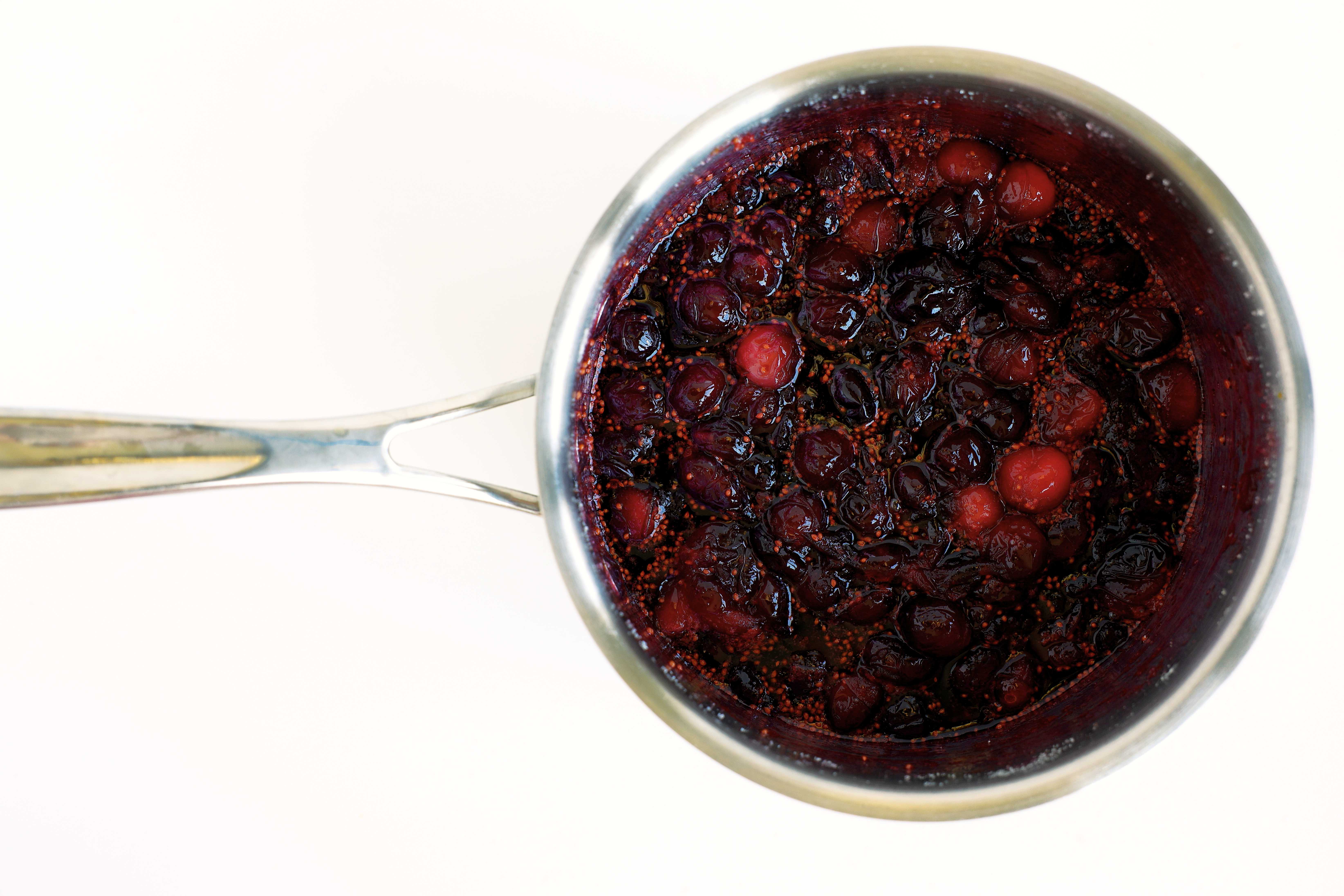 Overhead view of cooked cranberries in a saucepan, glossy and bursting after simmering.