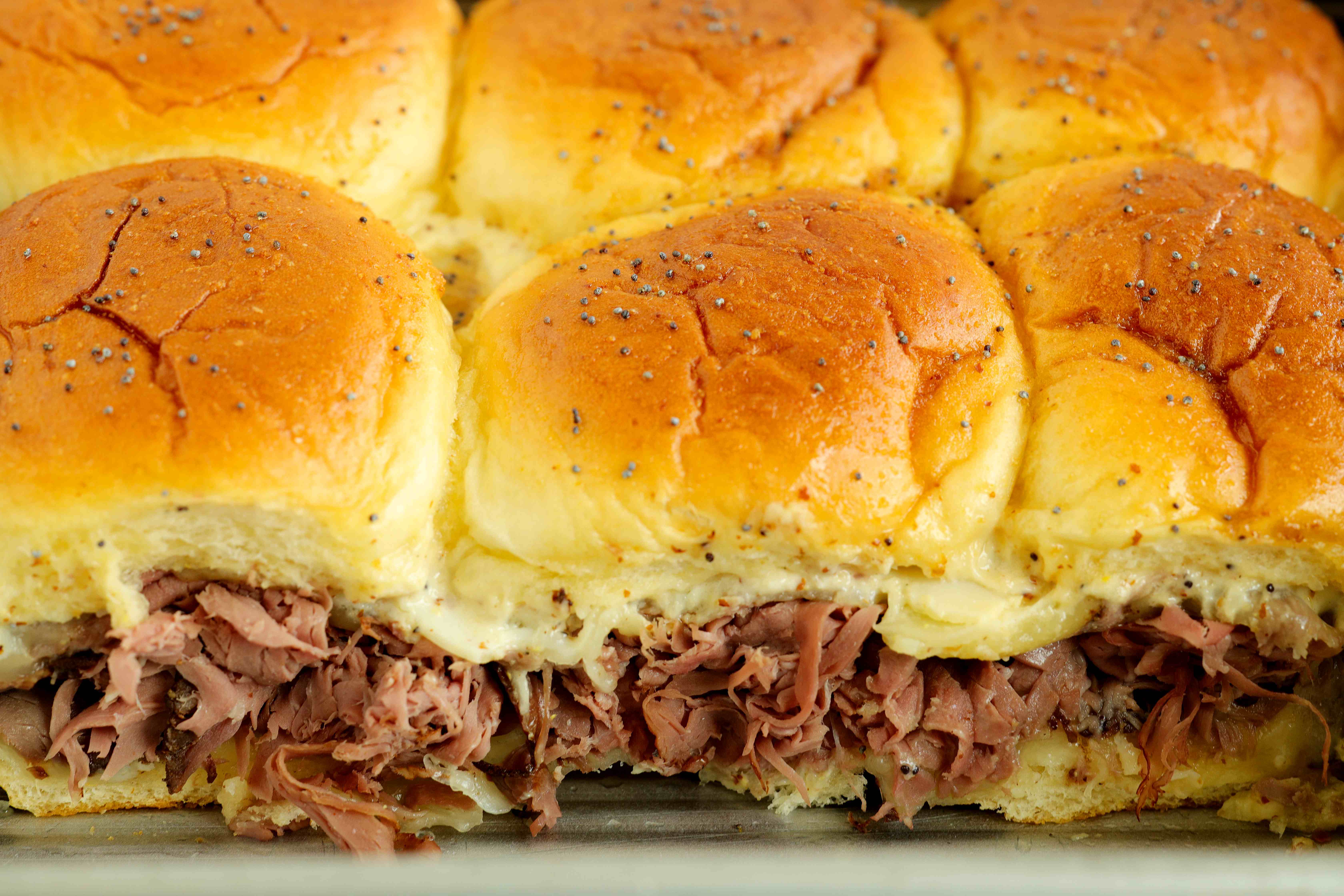Side view of baked roast beef sliders showing melted cheese and layers of roast beef.
