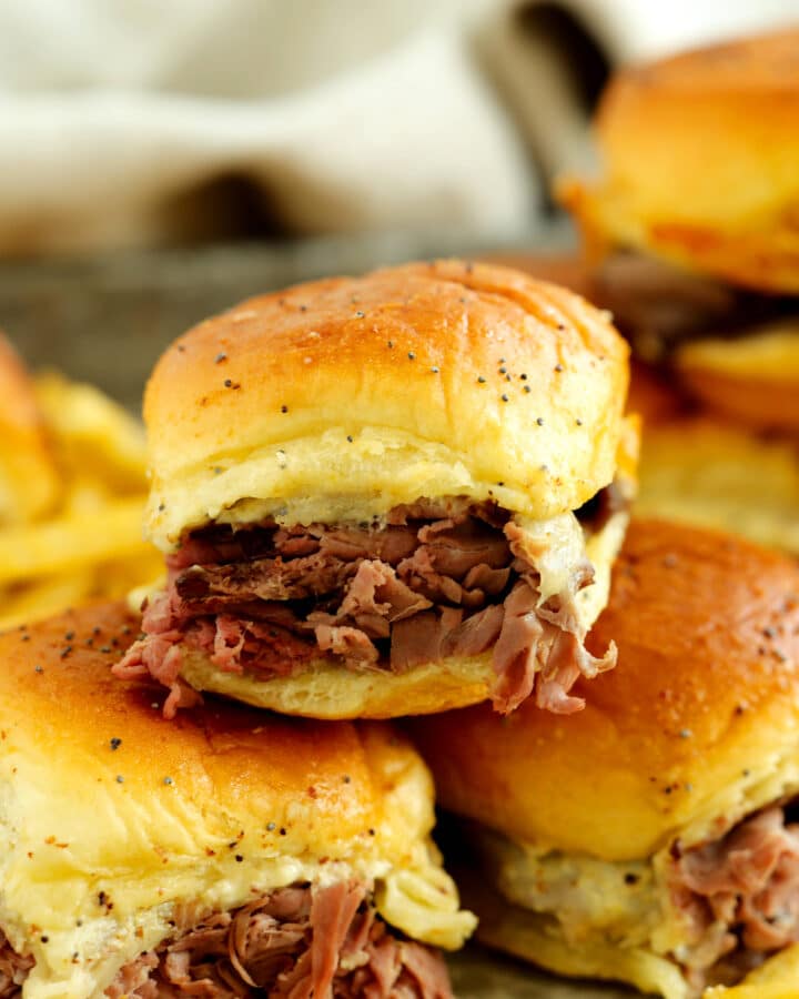 Stacked roast beef sliders with melted cheese on golden Hawaiian rolls served with fries.