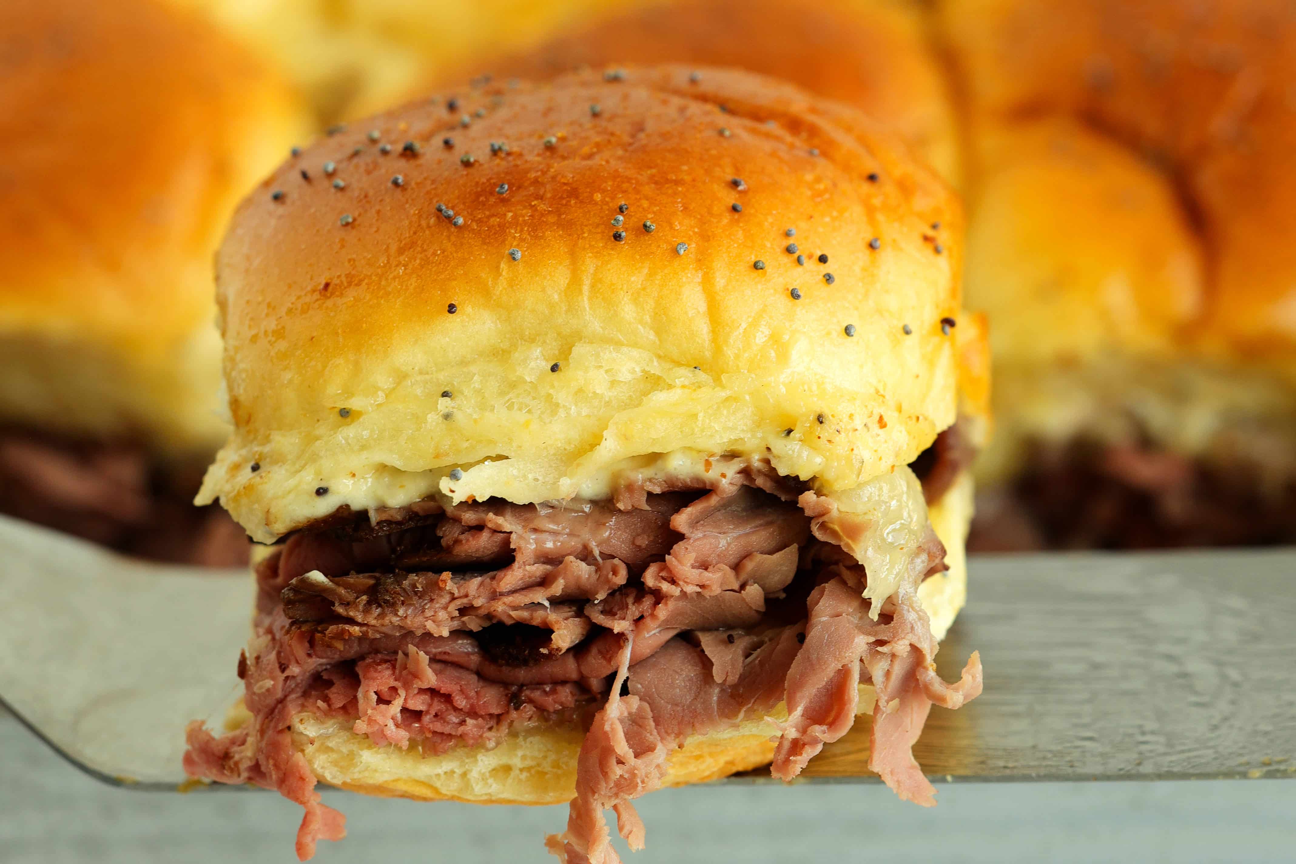 Close-up of a roast beef slider on a Hawaiian roll with melted provolone and poppy seed topping.