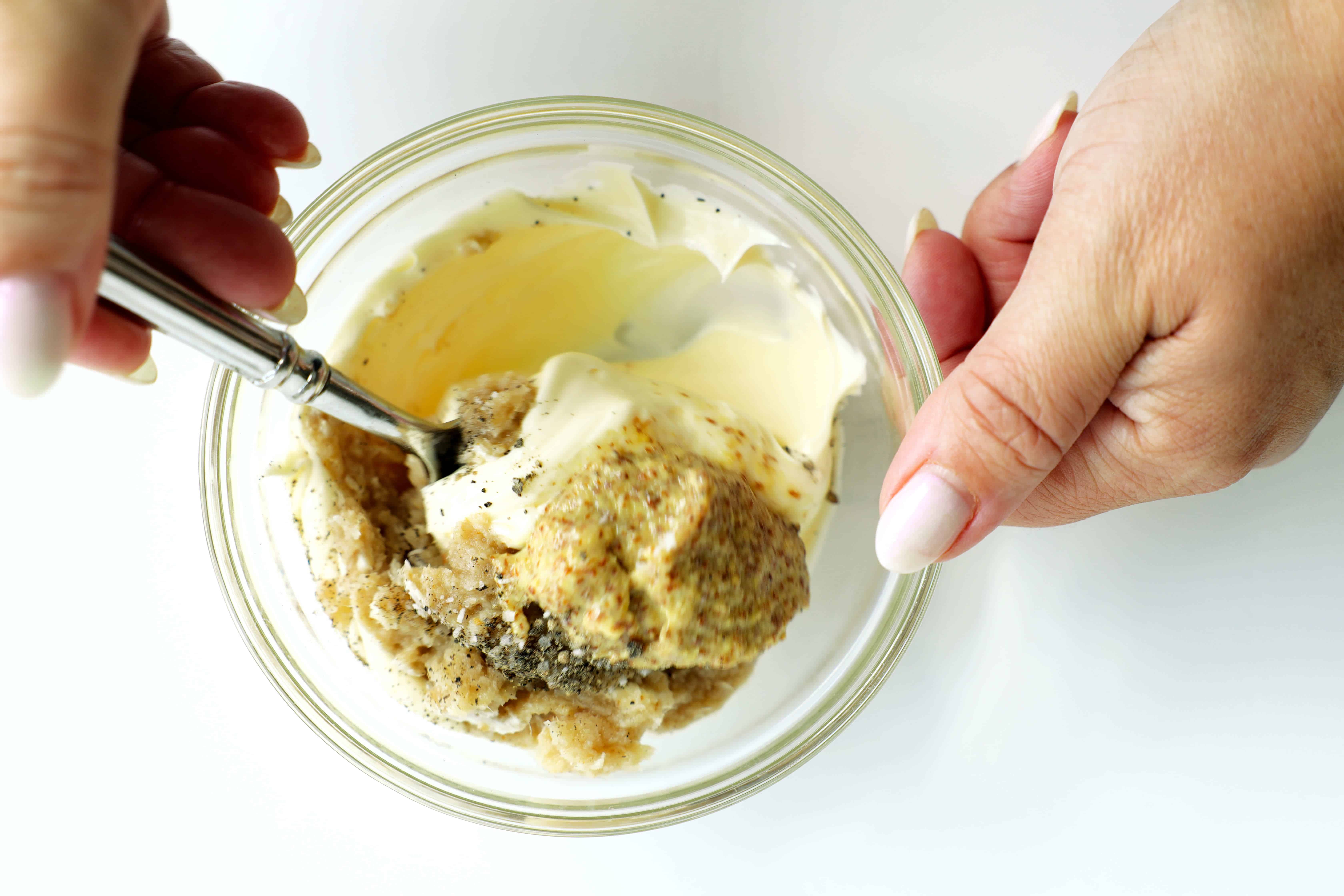 Mixing mayonnaise, horseradish, Dijon mustard, salt, and pepper in a glass bowl to make creamy horseradish sauce for roast beef sliders.