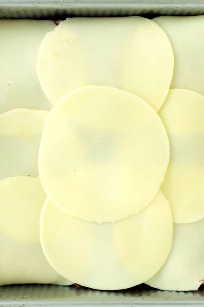 Layer of provolone cheese slices arranged on Hawaiian rolls for roast beef sliders.