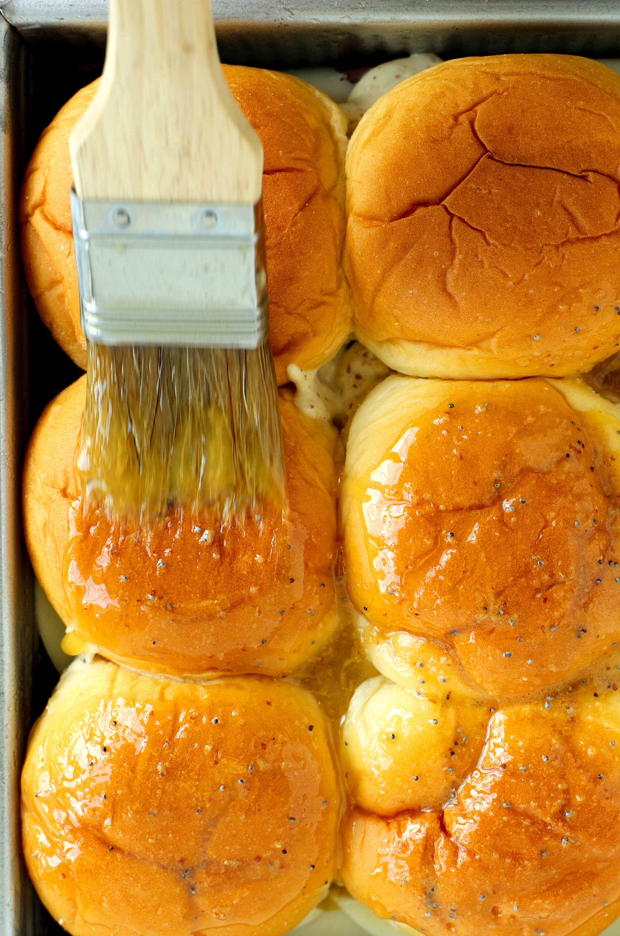 Brushing savory butter glaze over Hawaiian rolls for roast beef sliders before baking.
