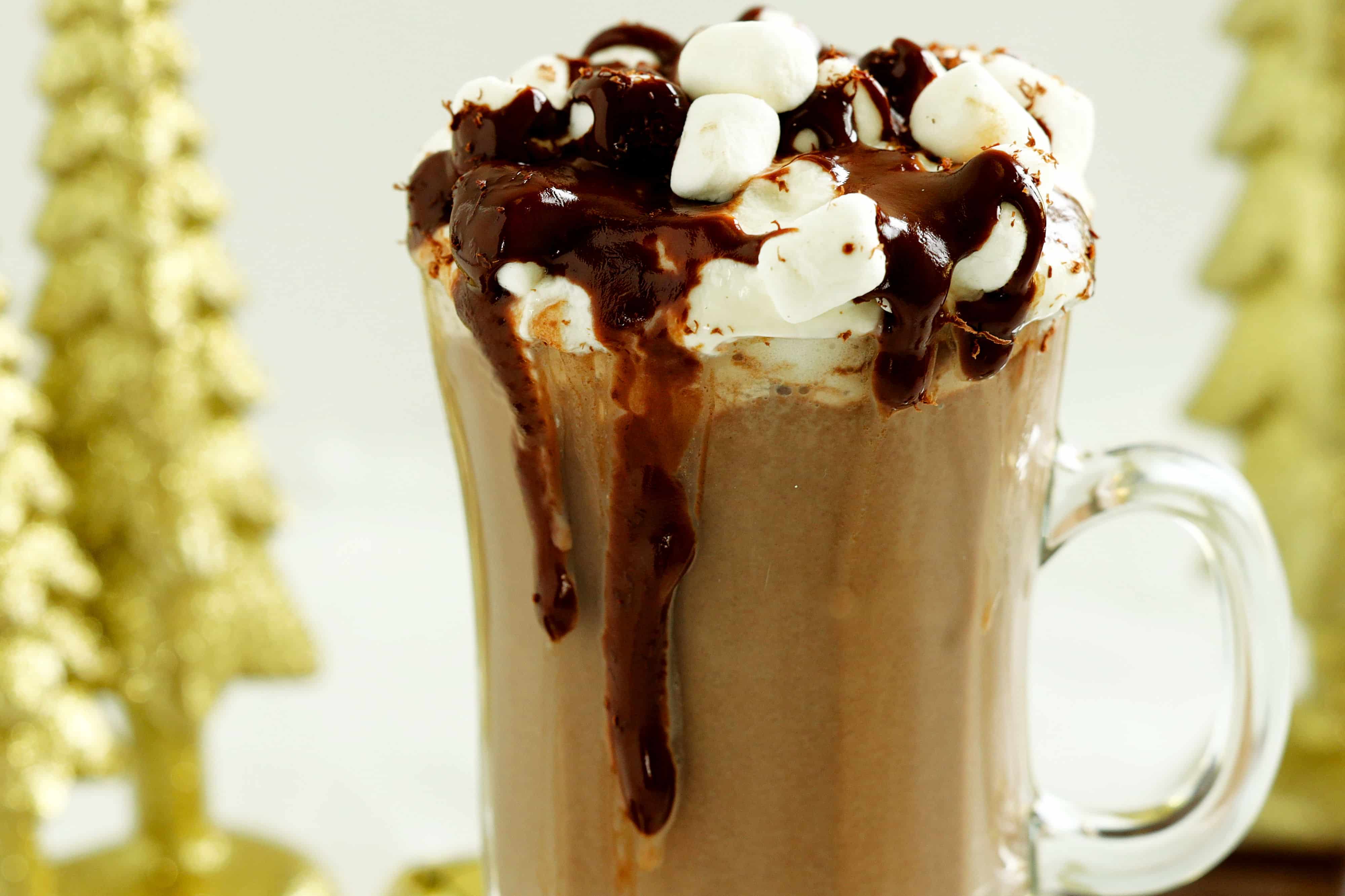 Close-up of whipped-cream&ndash;topped dark hot chocolate with mini marshmallows and glossy chocolate sauce dripping down the mug.