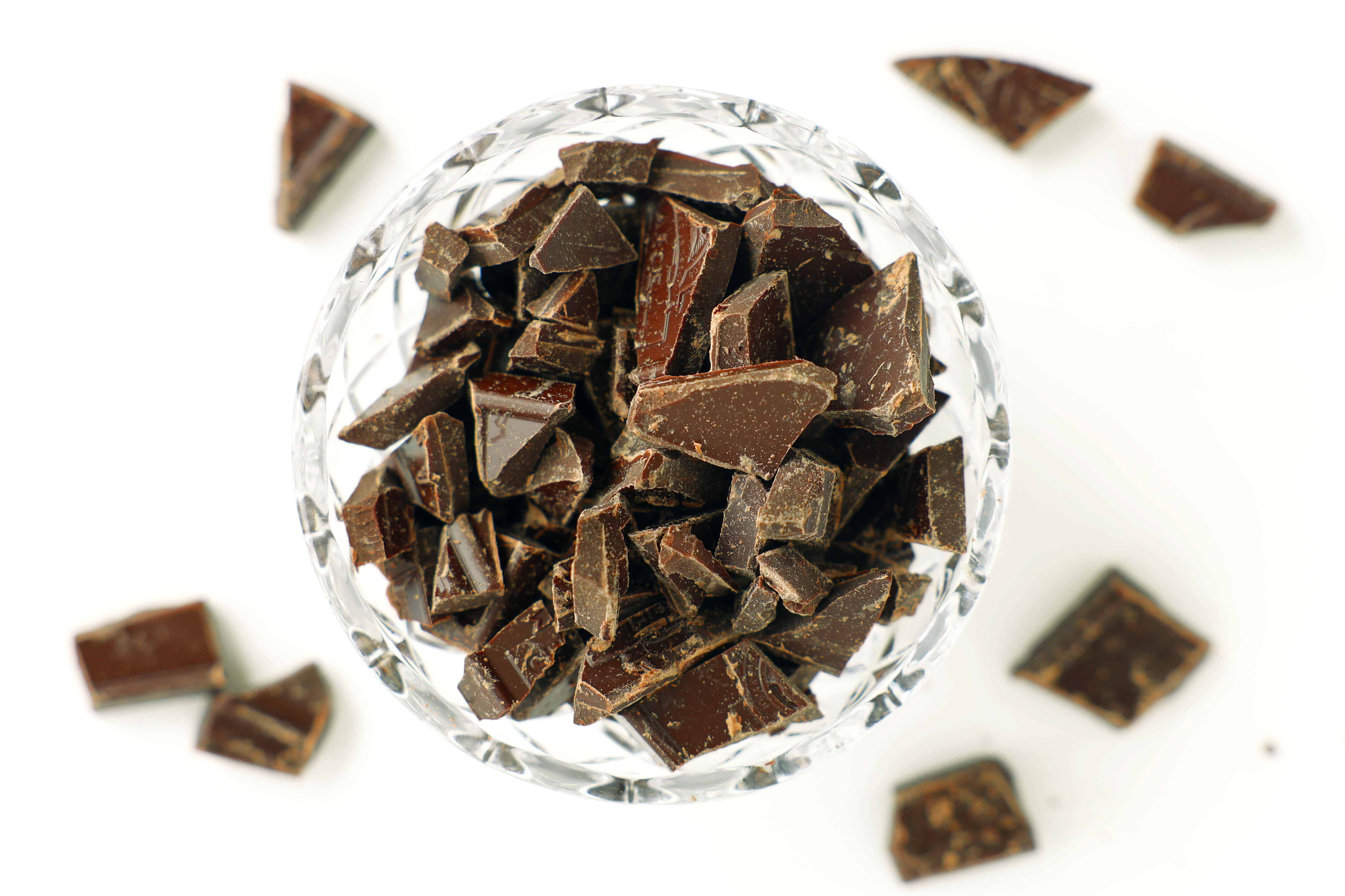 Cut-glass bowl filled with chopped dark chocolate pieces; a few shards scattered on a white surface.