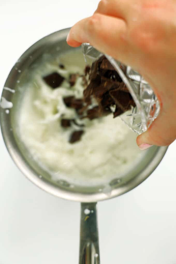 Adding chopped dark chocolate to hot milk in a saucepan to melt.
