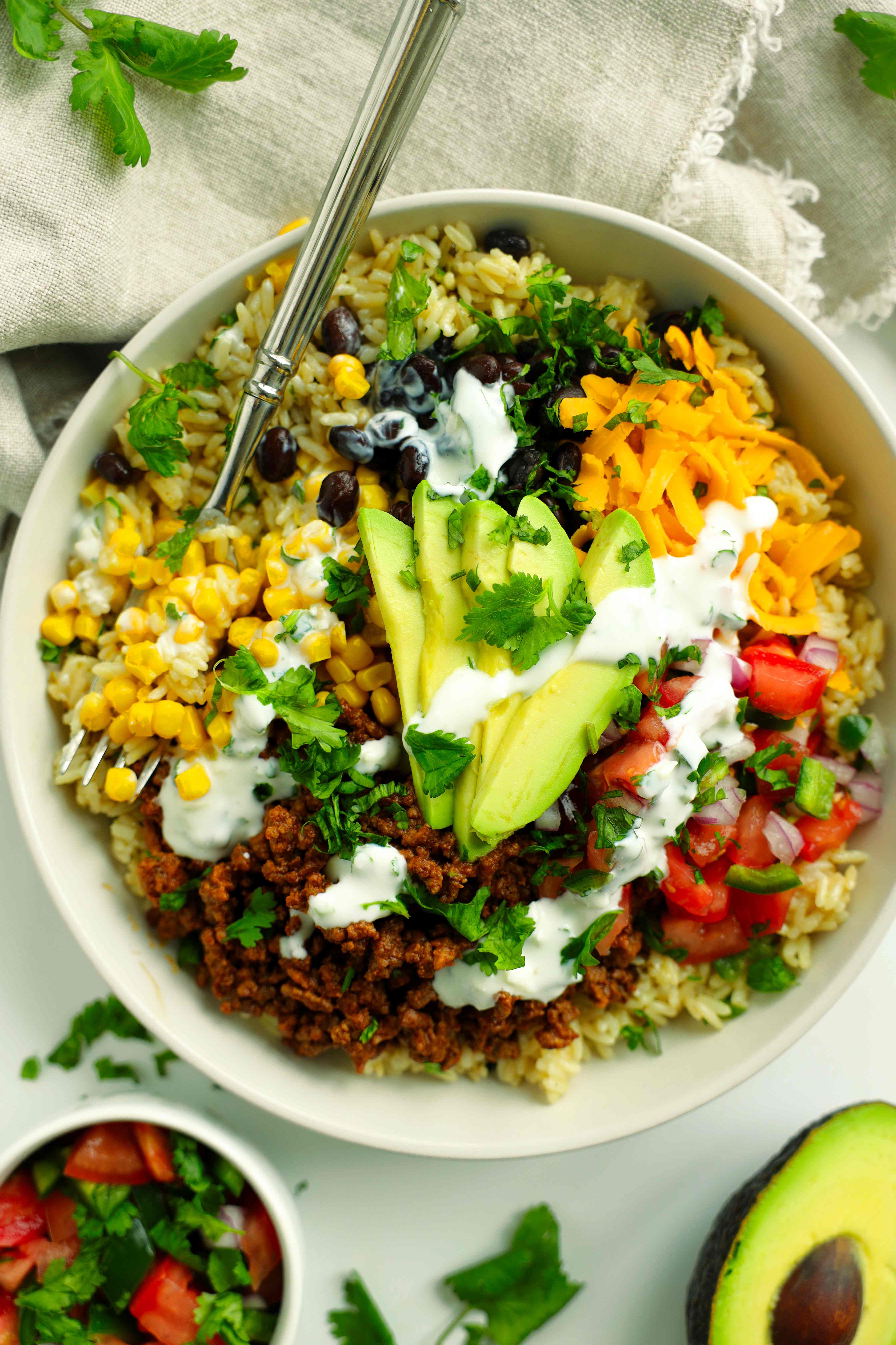 Easy beef taco bowl topped with avocado, cheese, pico de gallo, and creamy cilantro sauce