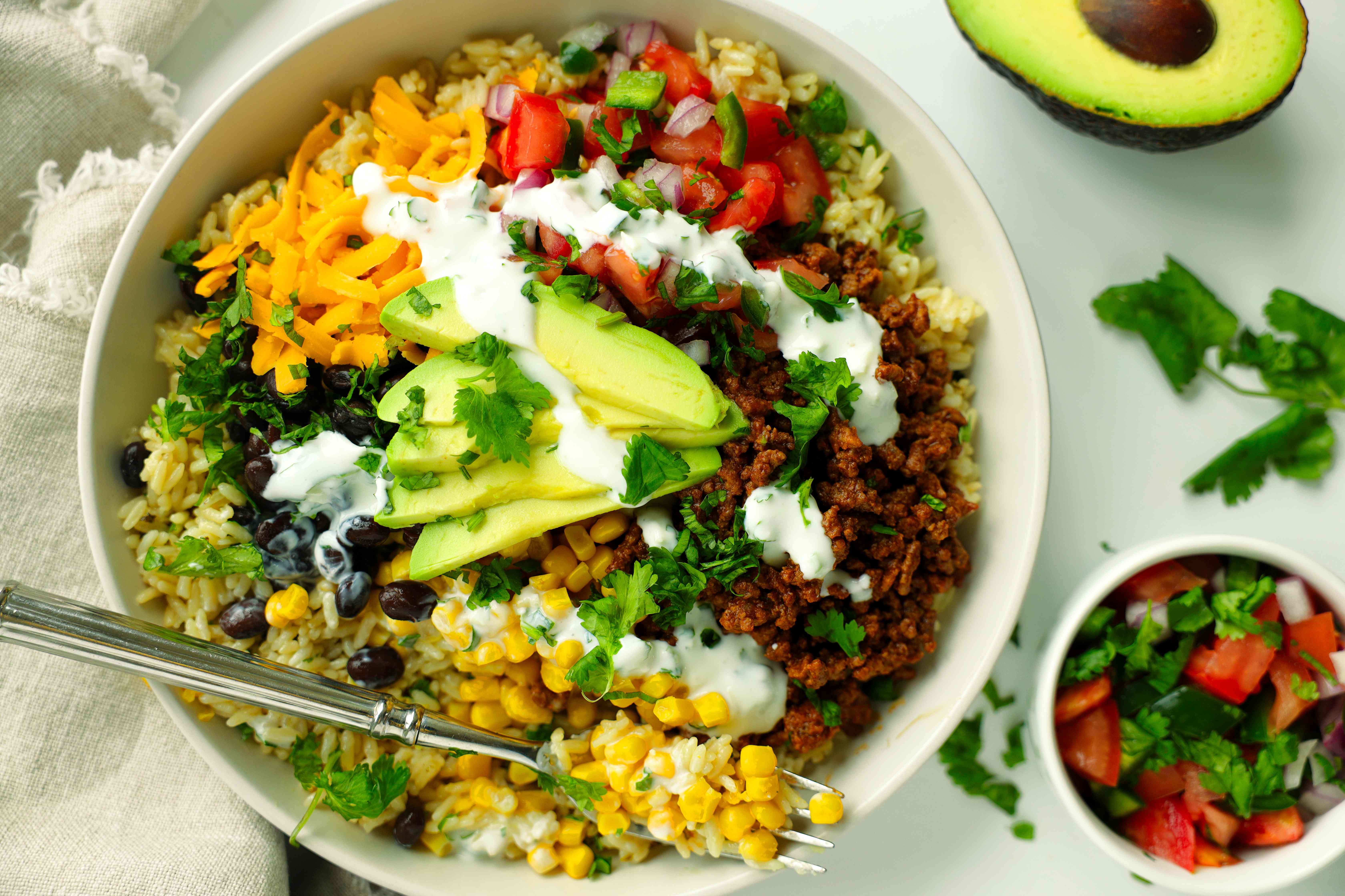 Easy beef taco bowl topped with avocado, cheese, pico de gallo, and creamy cilantro sauce