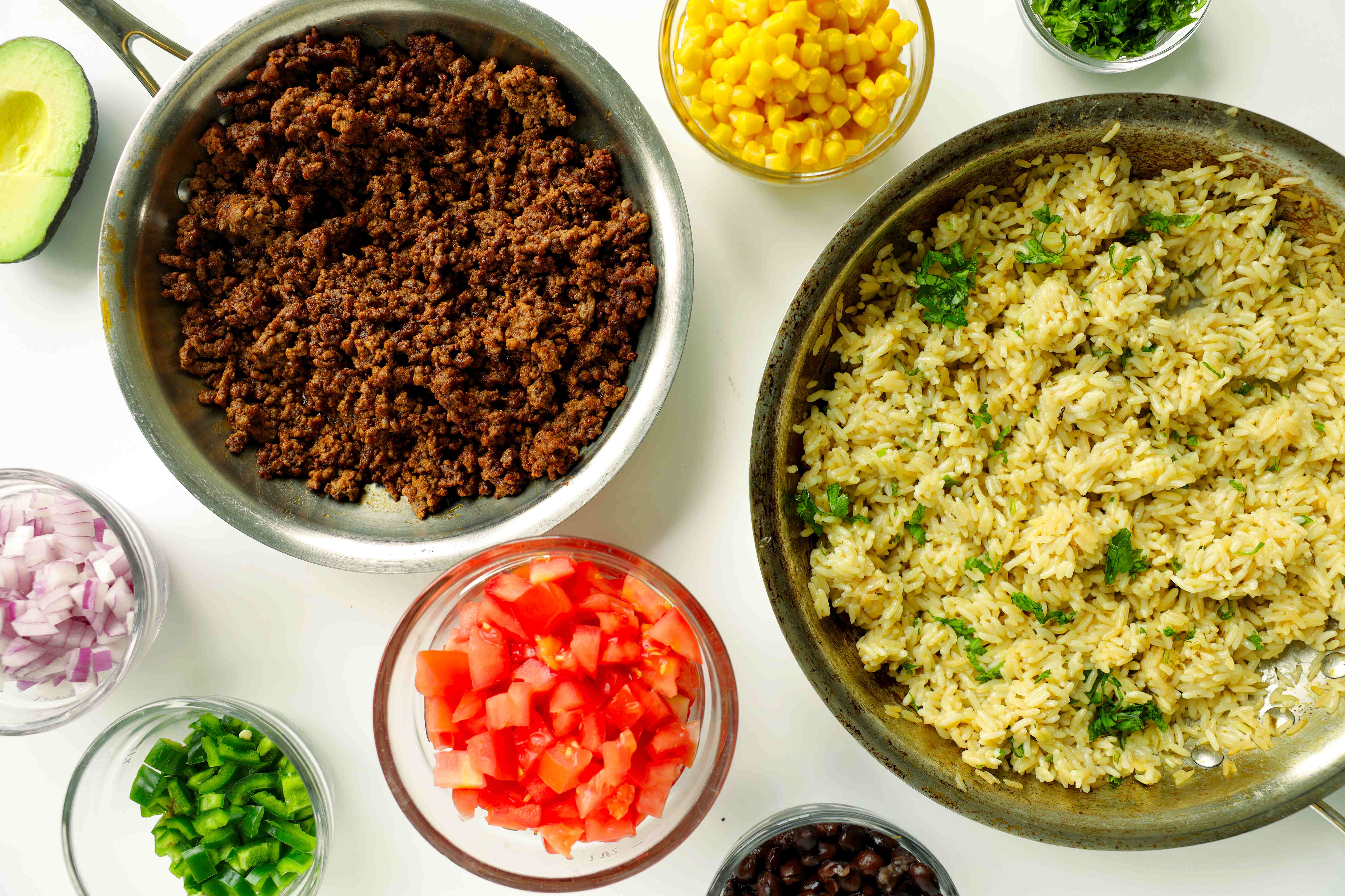 Taco bowl toppings in bowls including tomatoes, onions, peppers, and cilantro
