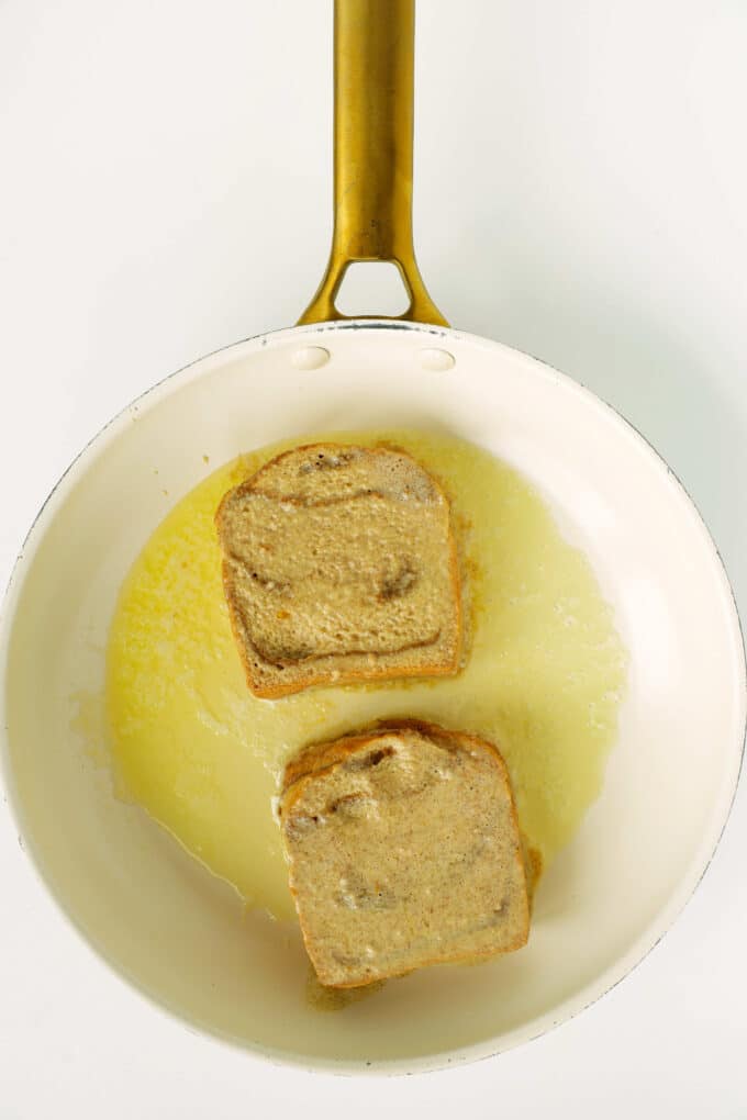 Brioche slices cooking in melted butter in a skillet.