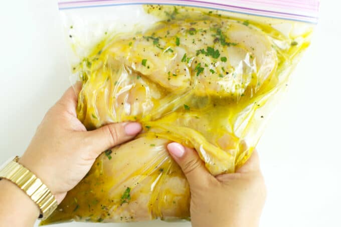 Massaging chicken in a zip-top bag with a garlic herb marinade to coat evenly before marinating