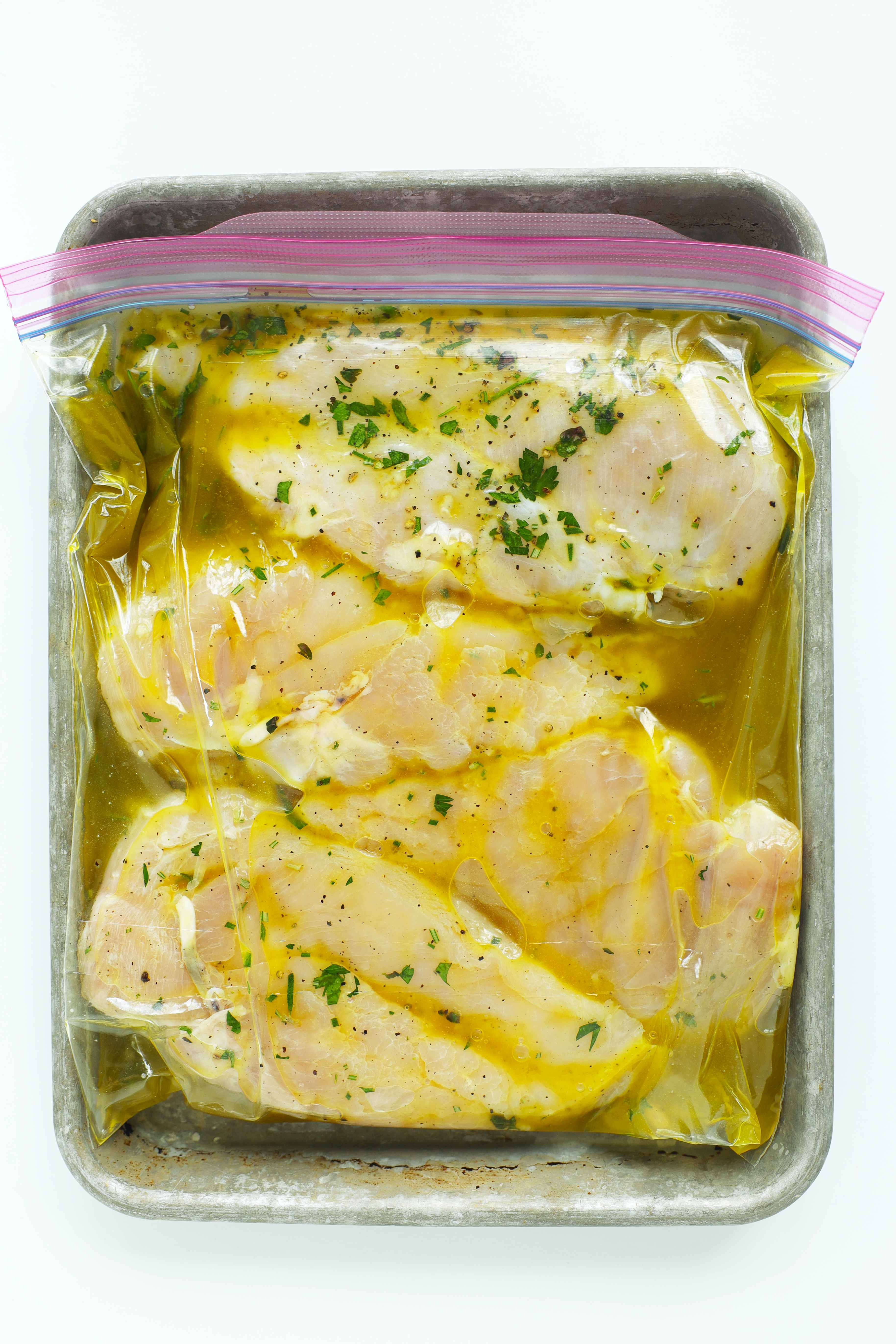 Chicken breasts marinating in a garlic herb marinade in a zip-top bag placed on a baking dish