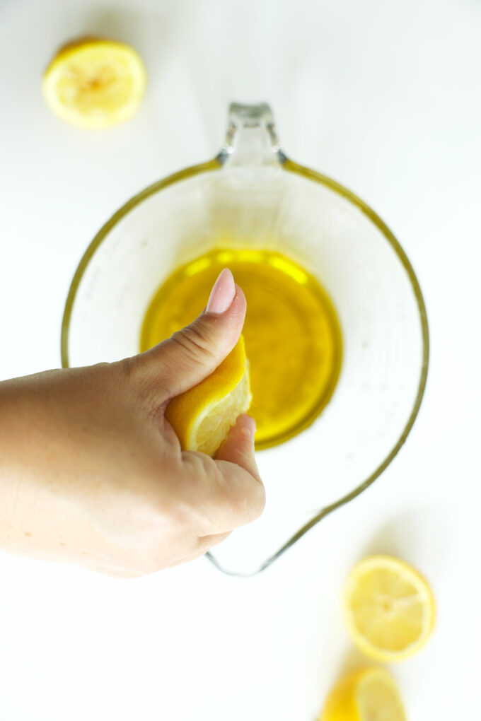Squeezing fresh lemon juice into olive oil for a bright and flavorful chicken marinade