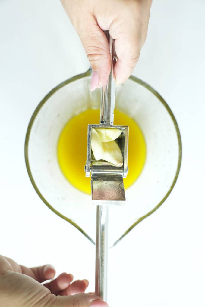 Pressing fresh garlic into a bowl of olive oil to make a flavorful chicken marinade