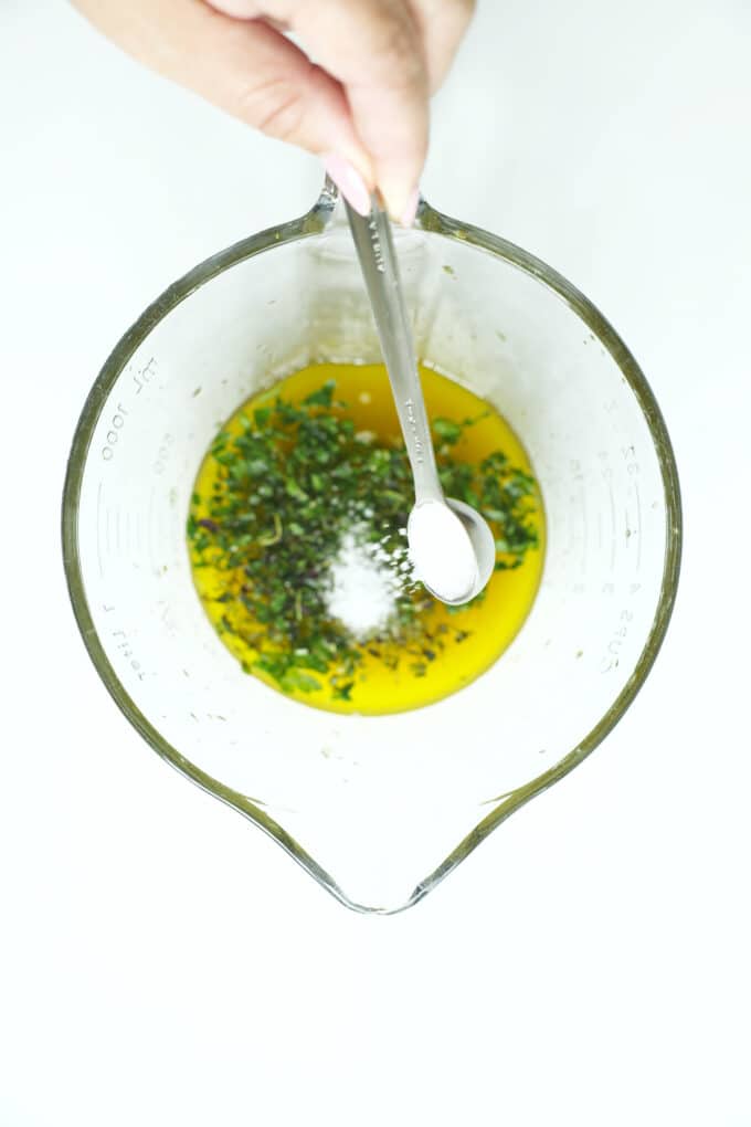 Adding salt and fresh herbs to a chicken marinade mixture of olive oil and lemon juice