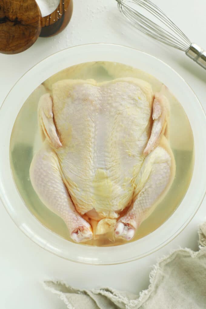 whole raw chicken sitting in chicken brine in clear glass bowl
