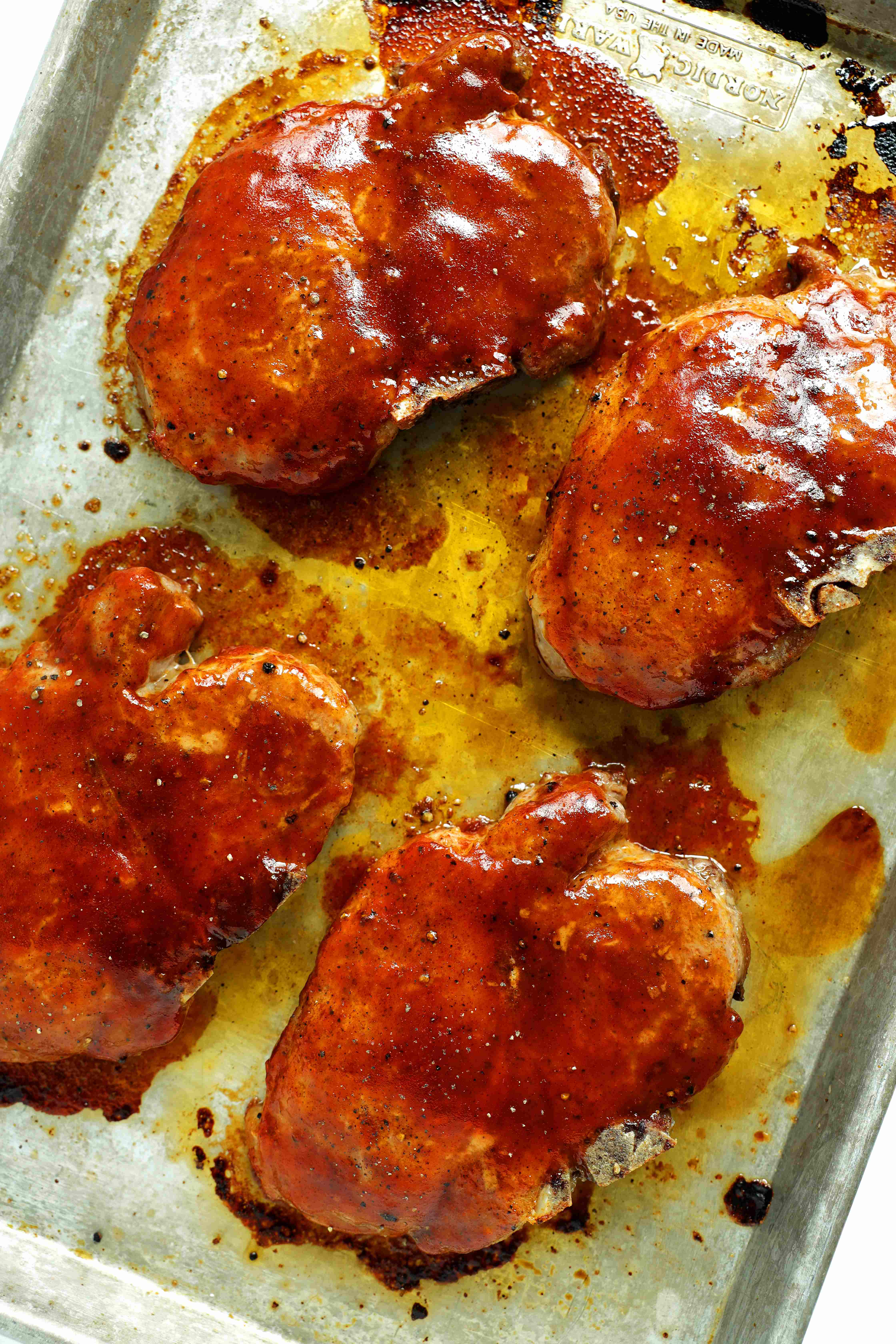 Overhead view of four baked BBQ pork chops coated with barbecue sauce on a sheet pan.